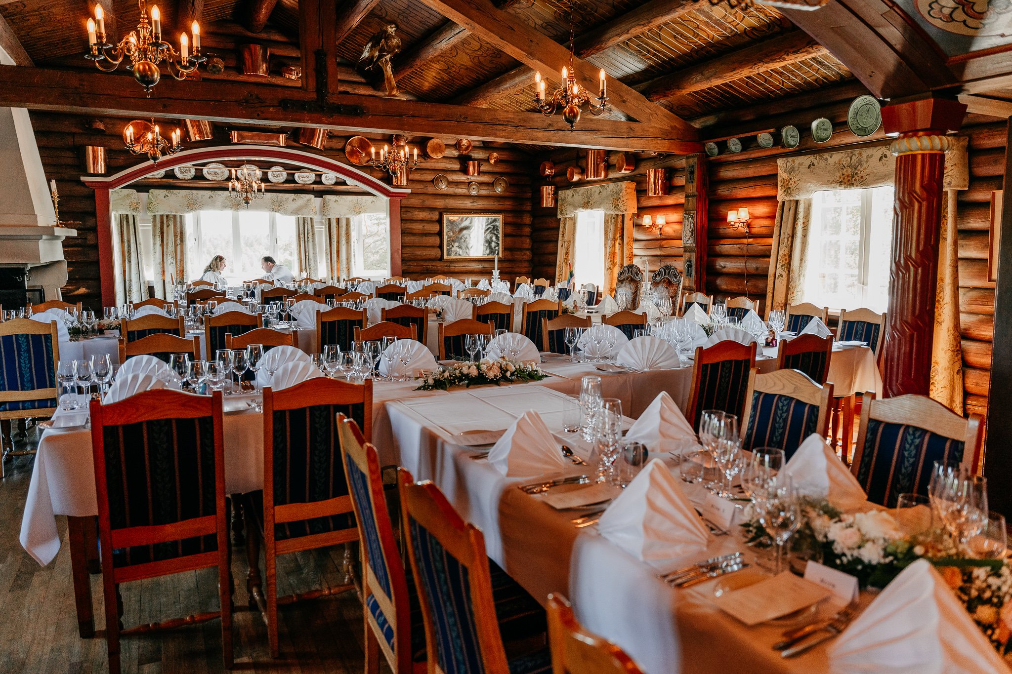 Ærverdig selskapslokale med tømmervegger og bord dekt med hvite duker.