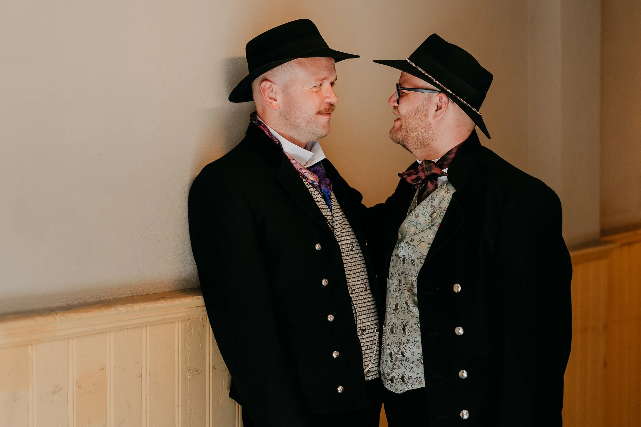 Two gooms standing against a wall almost about to kiss.
