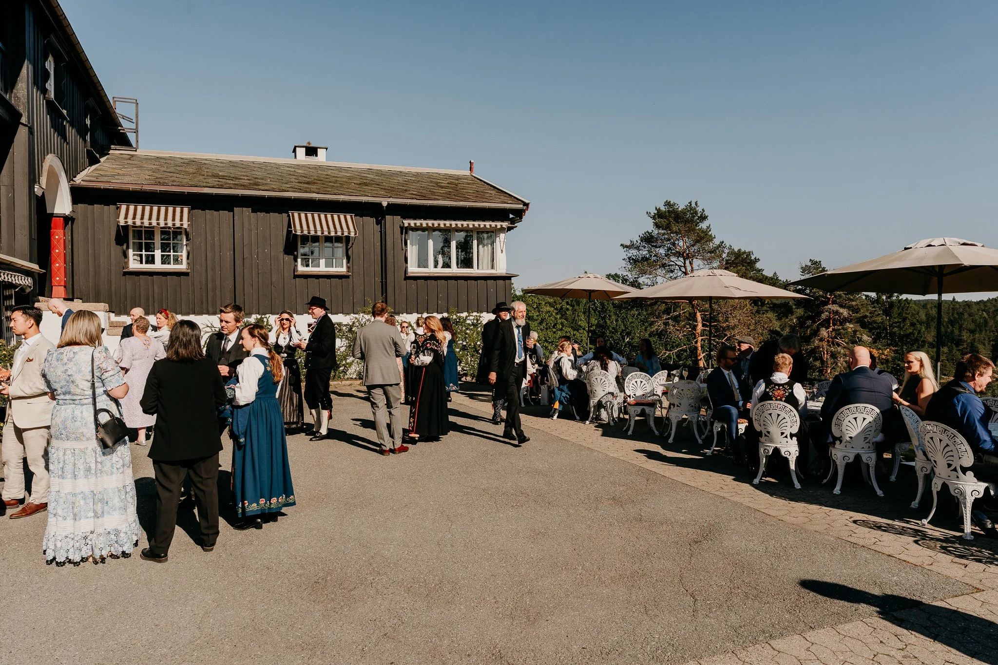 Mange mennesker utenfor et sortmalt bygg. Mange stoler og mennesker kledd i penklær.