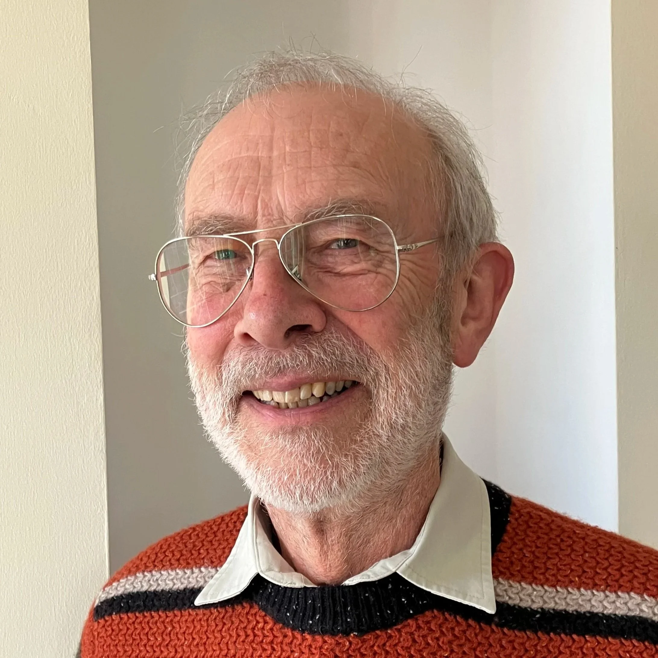 A grayscale portrait of a smiling man with glasses and a beard, resting his face on his hand.
