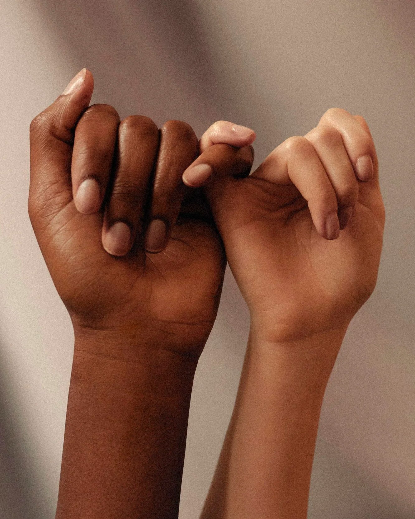 Two hands, one dark-skinned and one light-skinned, holding each other's pinky fingers.