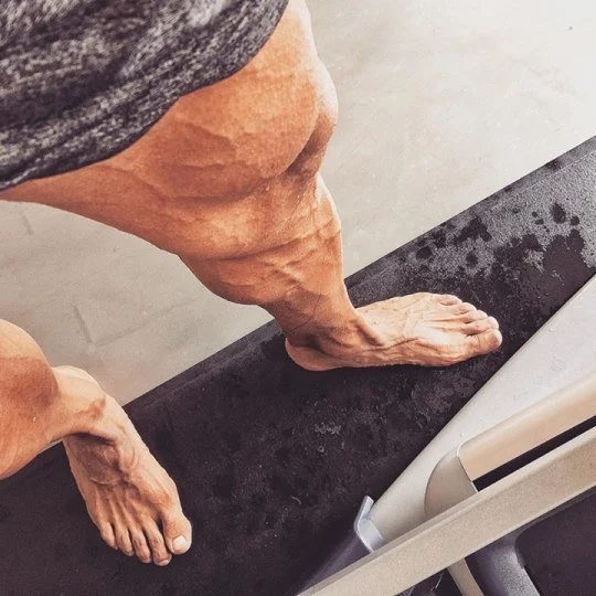 Close-up of a person's legs and feet standing on a treadmill.