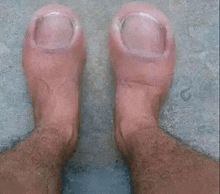 A pair of feet with toes and ankles, viewed from above, resting on a gray surface.