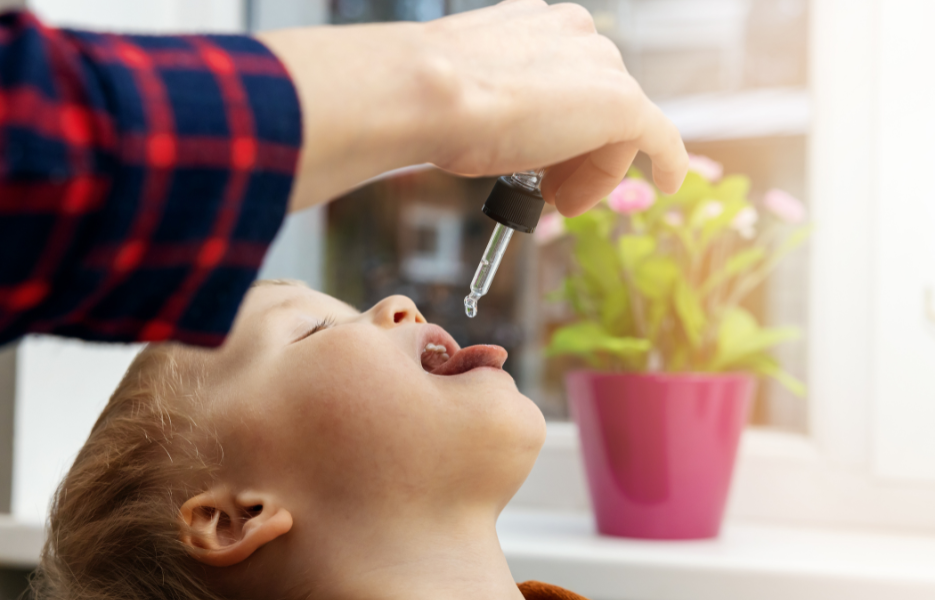 A young girl with closed eyes and open mouth receiving a drop of Bach Flower remedy from an adult using a dropper.