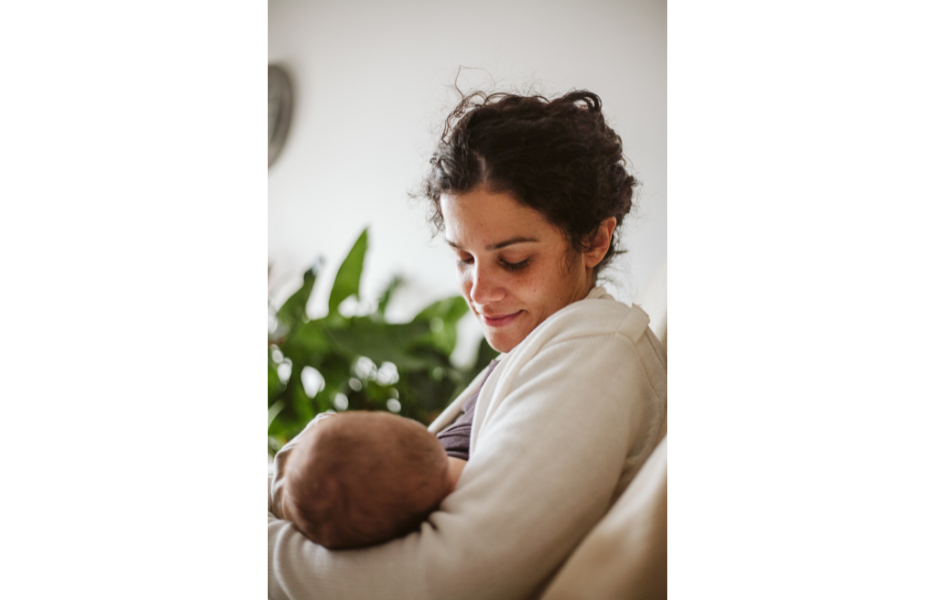 A woman breastfeeding, looking down at the baby with a gentle smile.