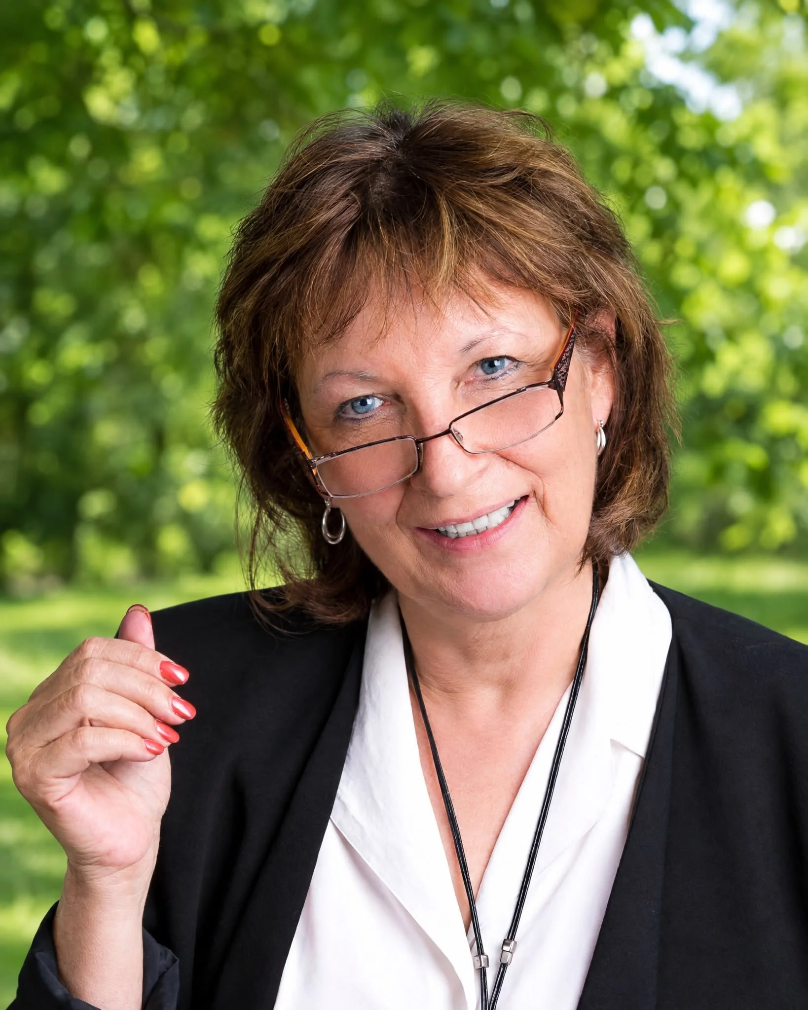 Headshot of a smiling woman with short reddish-brown hair, wearing a black blazer over a white blouse, and pearl earrings.