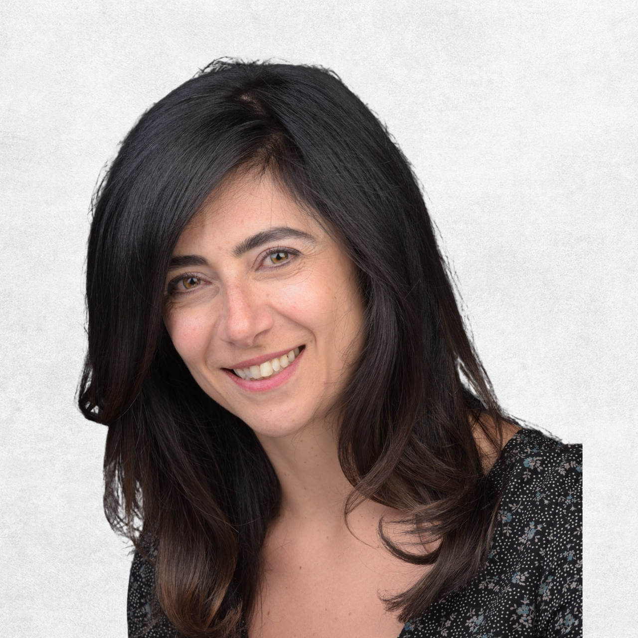 A woman with long dark hair, smiling, wearing a black patterned top, with a light gray background.