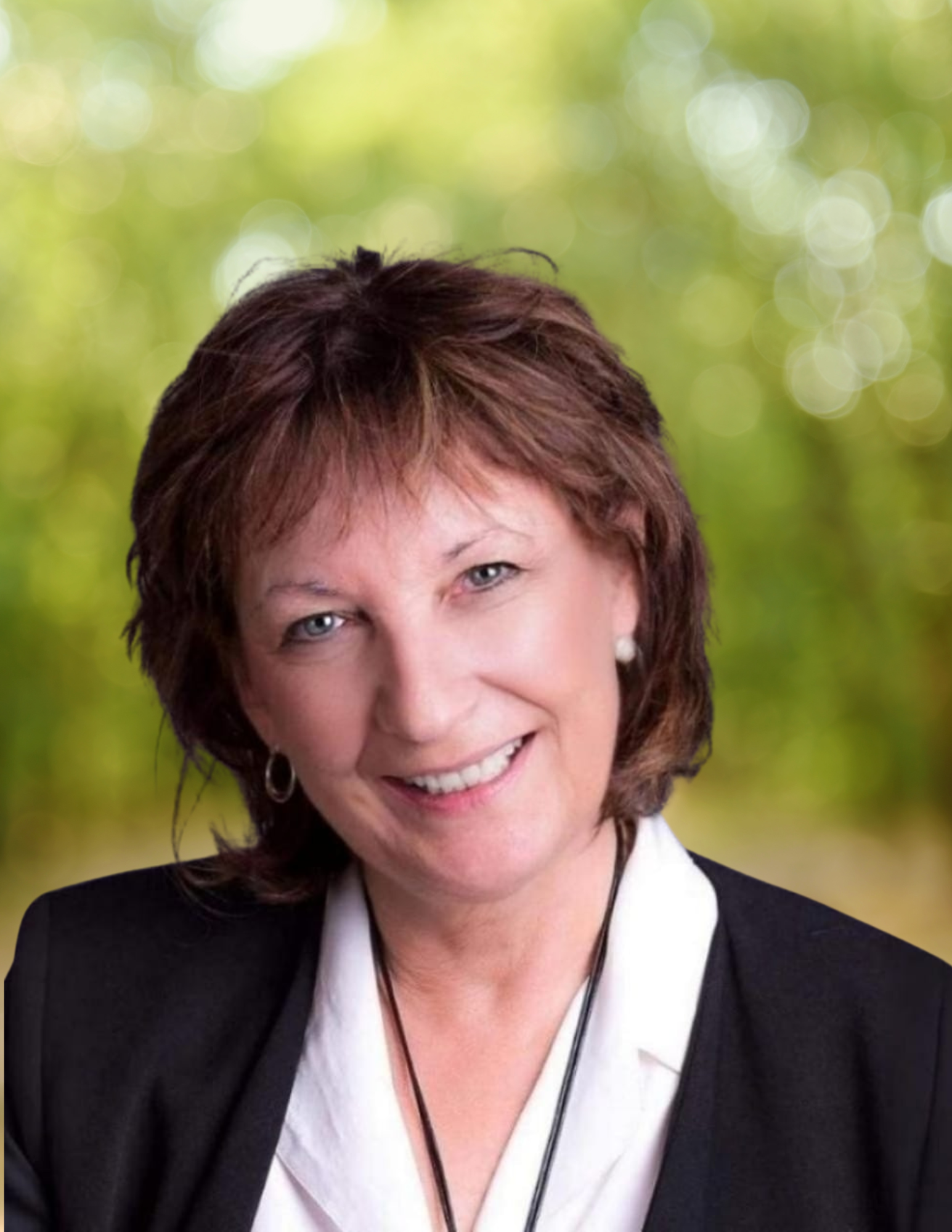 Headshot of a smiling woman with short reddish-brown hair, wearing a black blazer over a white blouse, and pearl earrings.