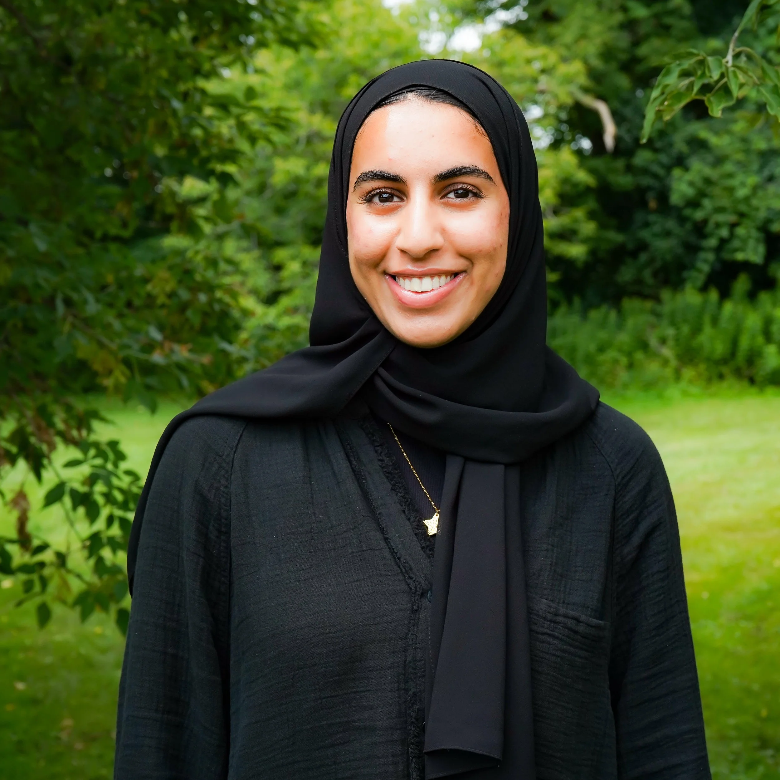 A young woman with light skin wearing a beige hijab and earrings, smiling at the camera.