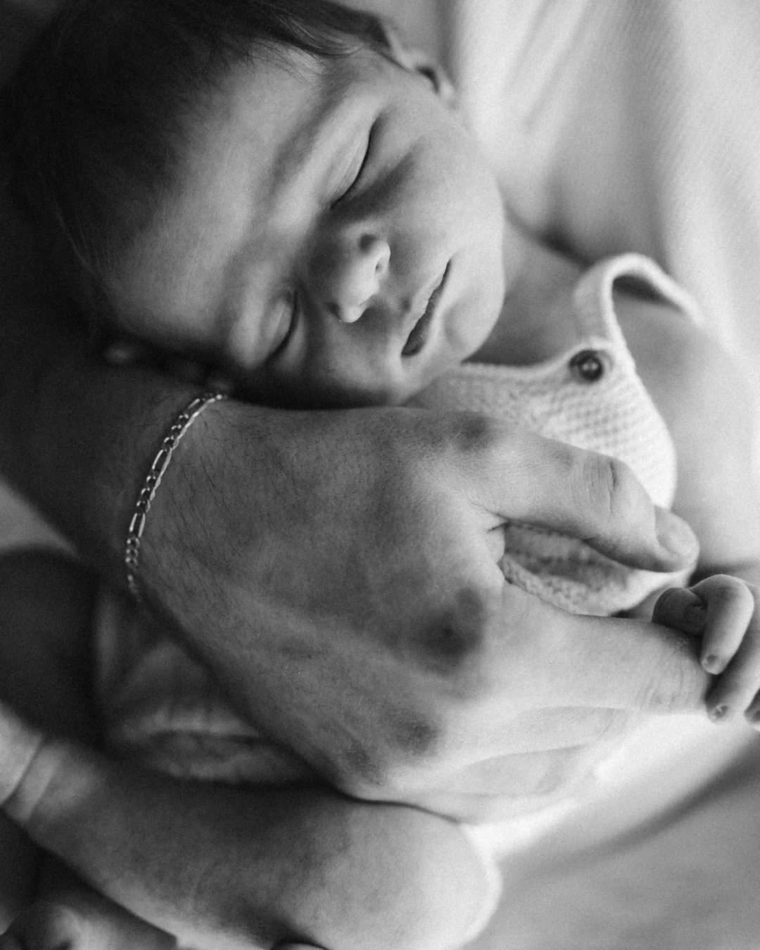 Ein schlafendes Baby, das in der Hand eines Erwachsenen ruht, in Schwarz-Weiß aufgenommen.