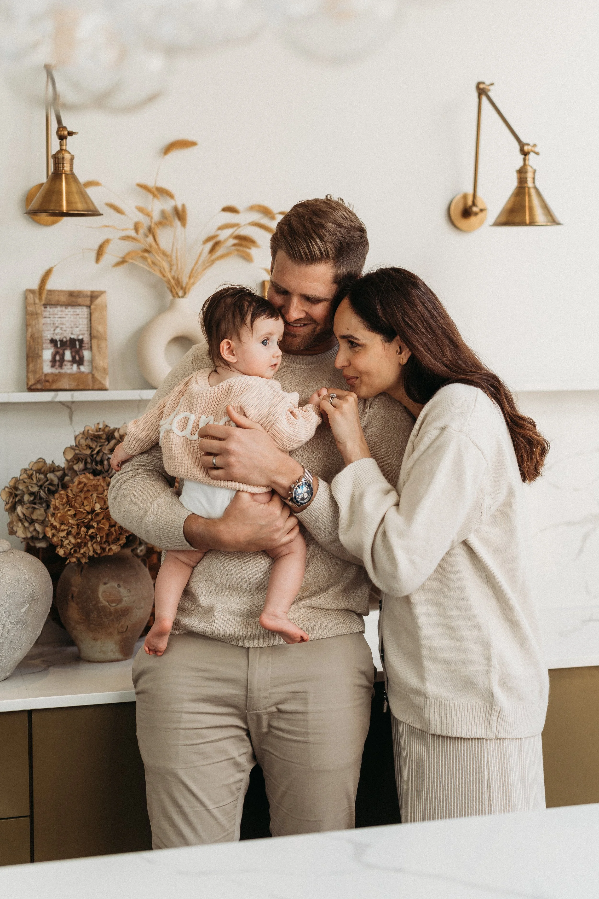 Familie mit zweijährigem Kind in einer hellem Raum, umarmend und lachend, mit Deko und Vasen im Hintergrund.
