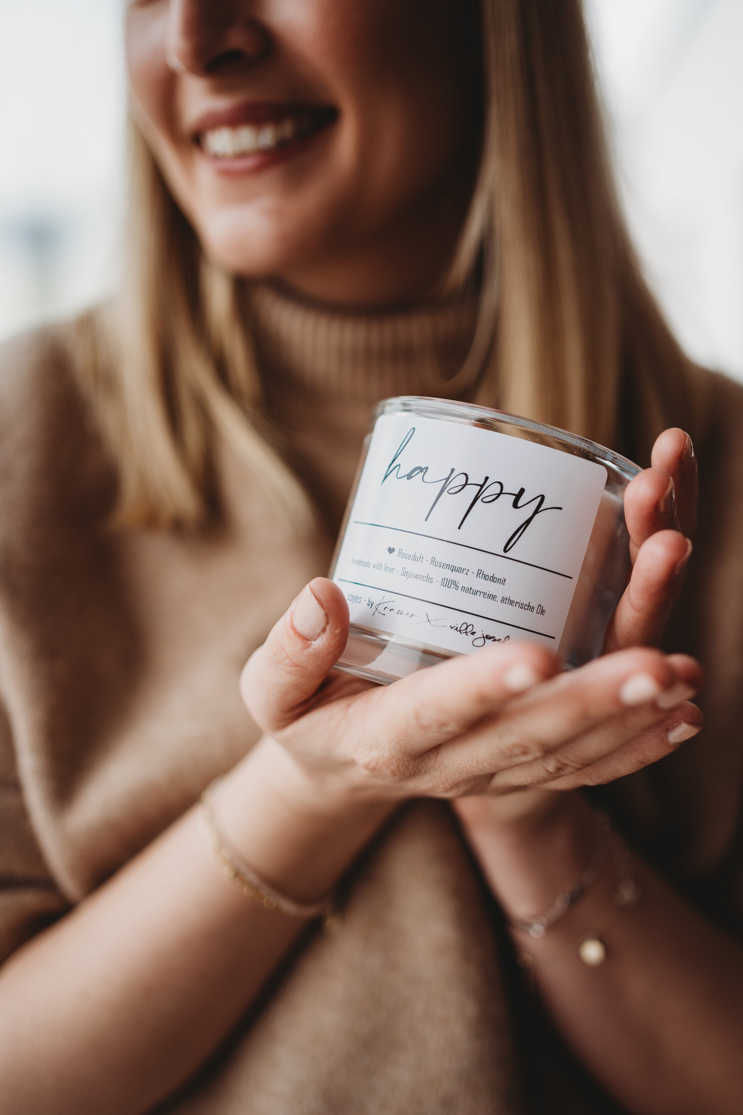 Nahaufnahme einer lächelnden Frau, die eine Kerze mit der Aufschrift 'happy' hält.