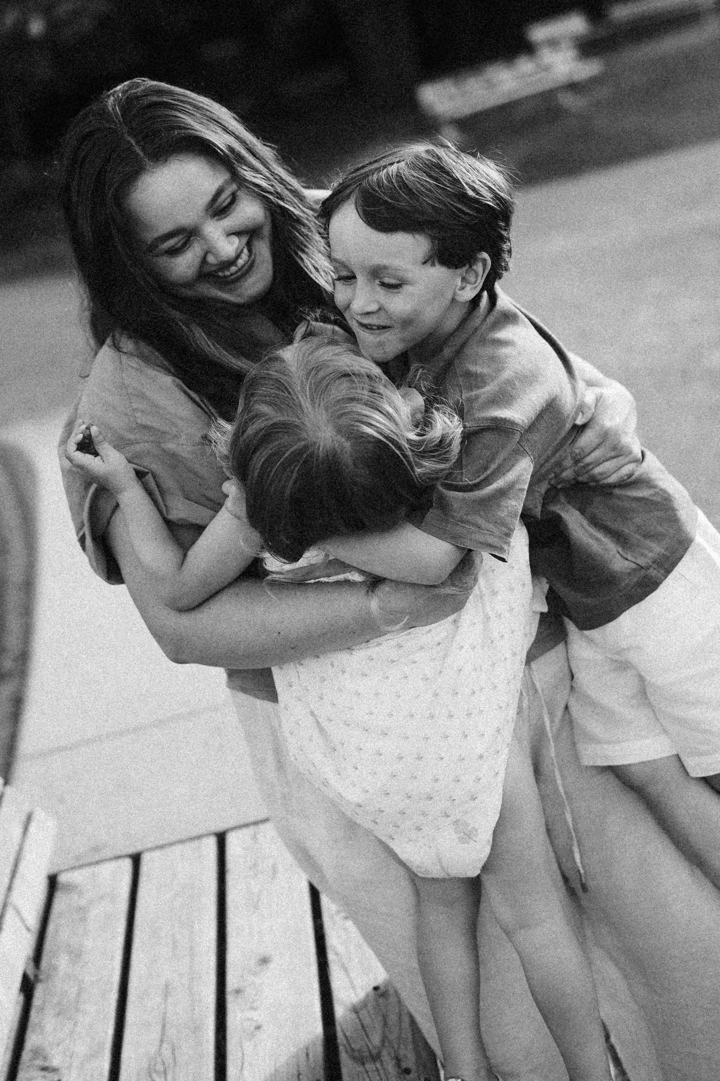 Ein schlichtes Schwarz-Weiß-Foto von vier Kindern, die sich umarmen und lächeln, auf einem Holzparkett, beim Spielen oder Kuscheln.