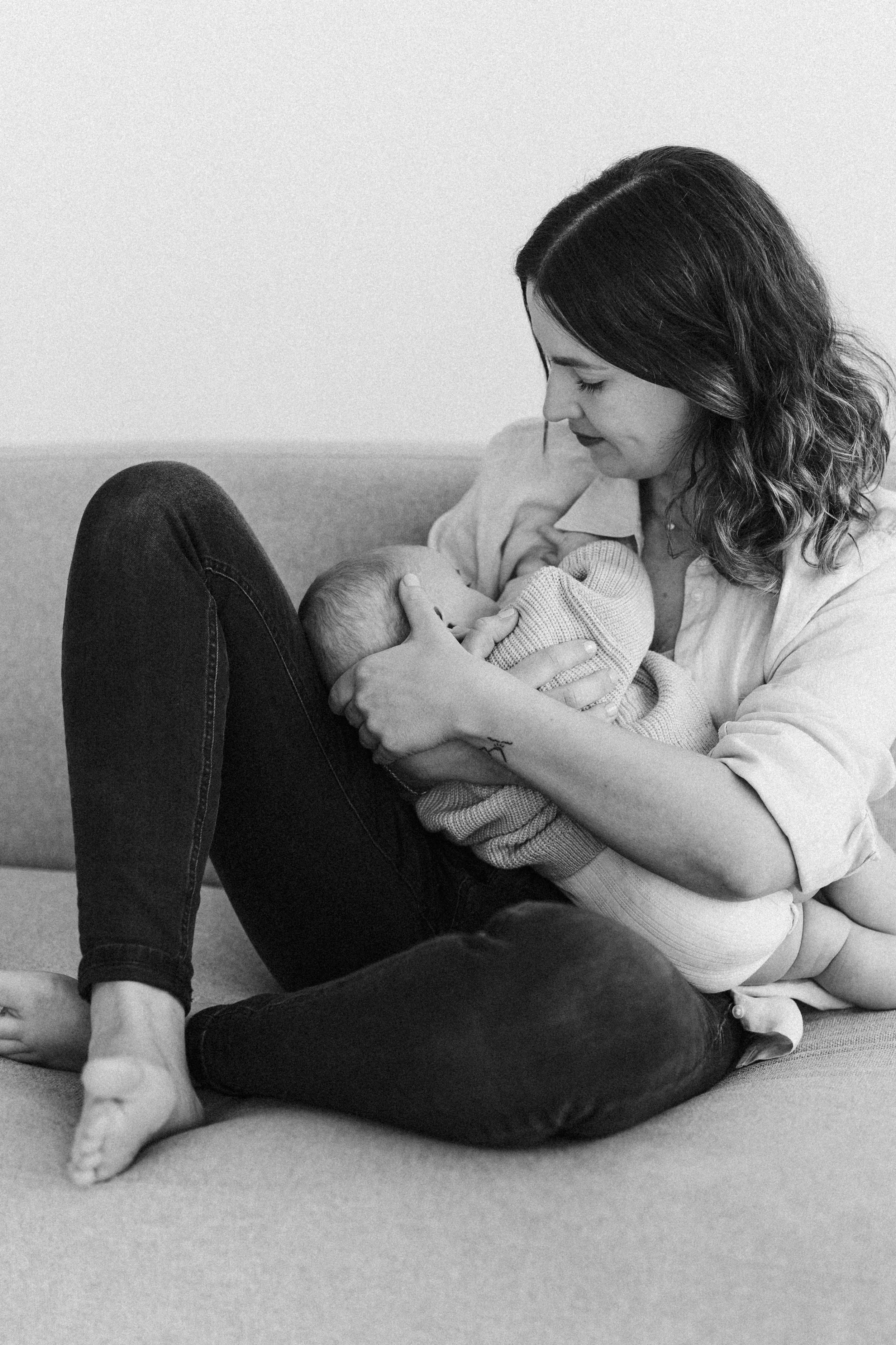 Eine Frau stillt ein Baby auf einem Sofa, in Schwarz-Weiß