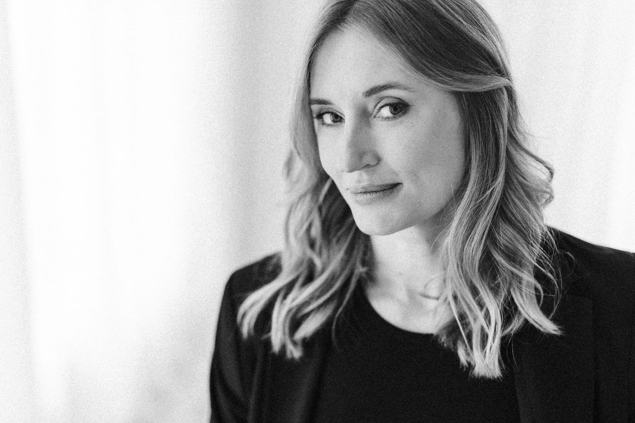 Schwarz-weiß-Porträt einer Frau mit welligem Schulterhaar und dunklem Oberteil, blickt leicht zur Seite.