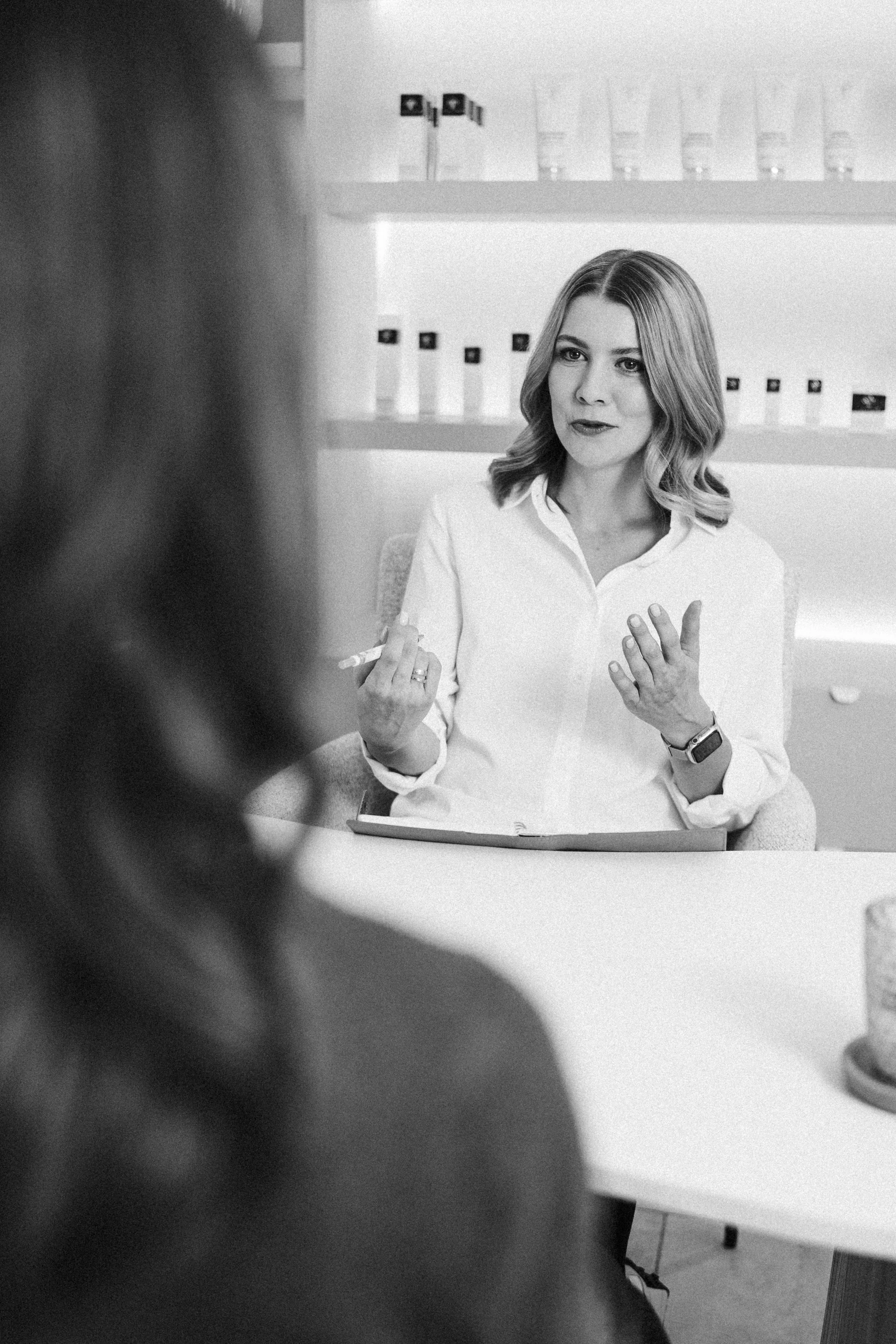 Junge Frau im Gespräch, im Hintergrund Produktregale, in Schwarz-Weiß.