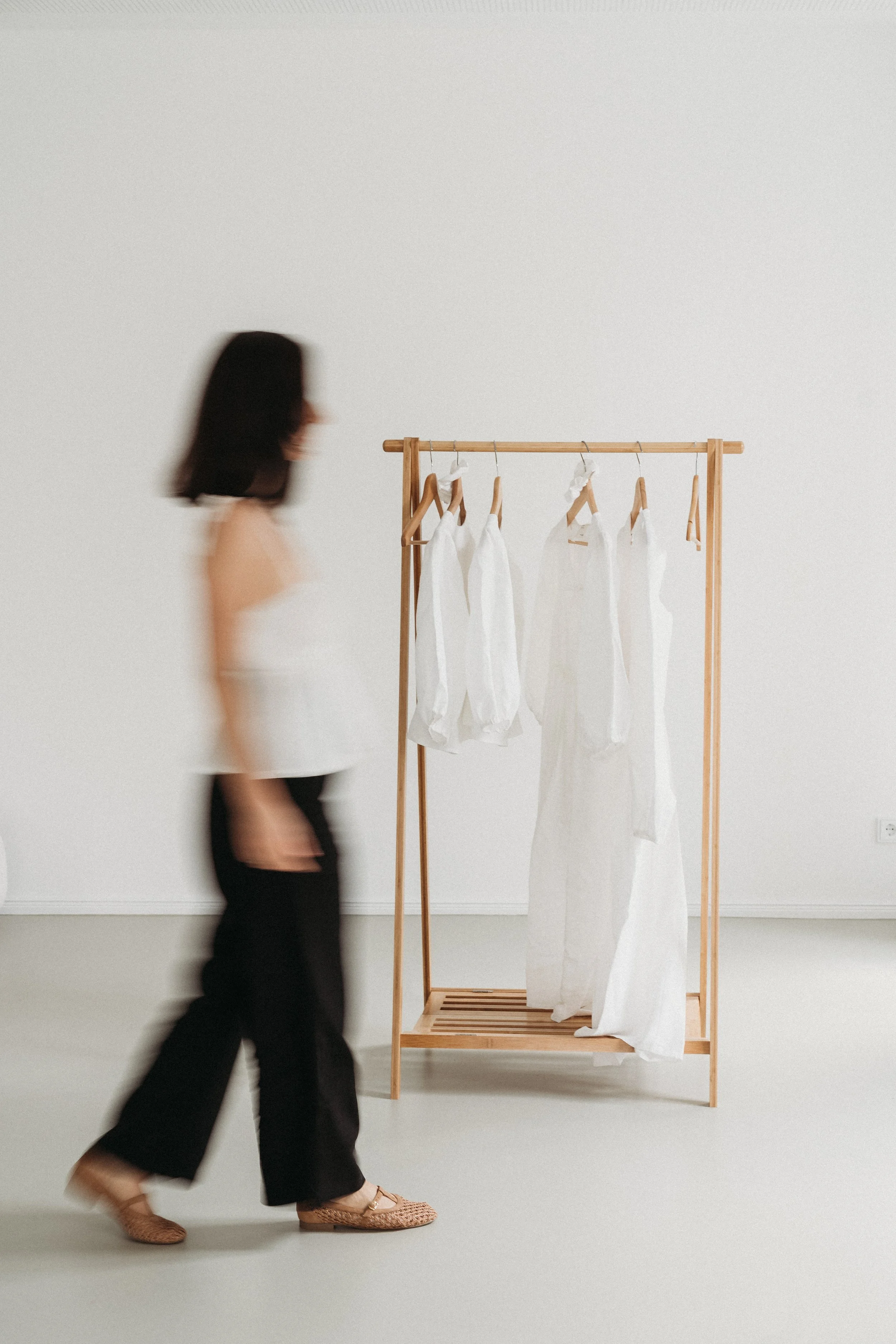 Frau geht an einem Kleiderständer mit weißen Kleidern vorbei in einem weißen Raum.