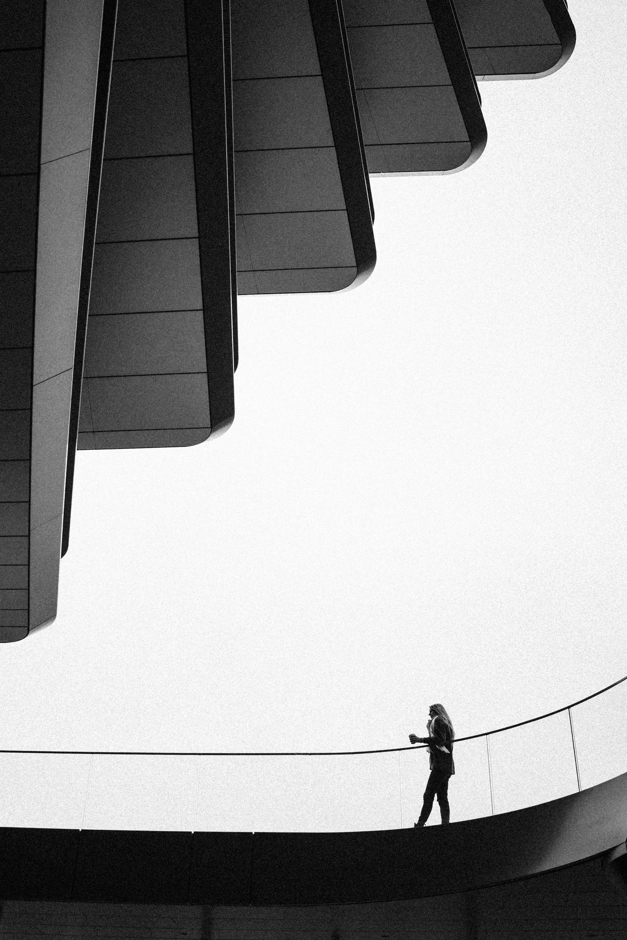 Schwarz-weiß-Fotografie einer Person, die auf einer runden Plattform geht, mit modernen architektonischen Strukturen im oberen Bildbereich.