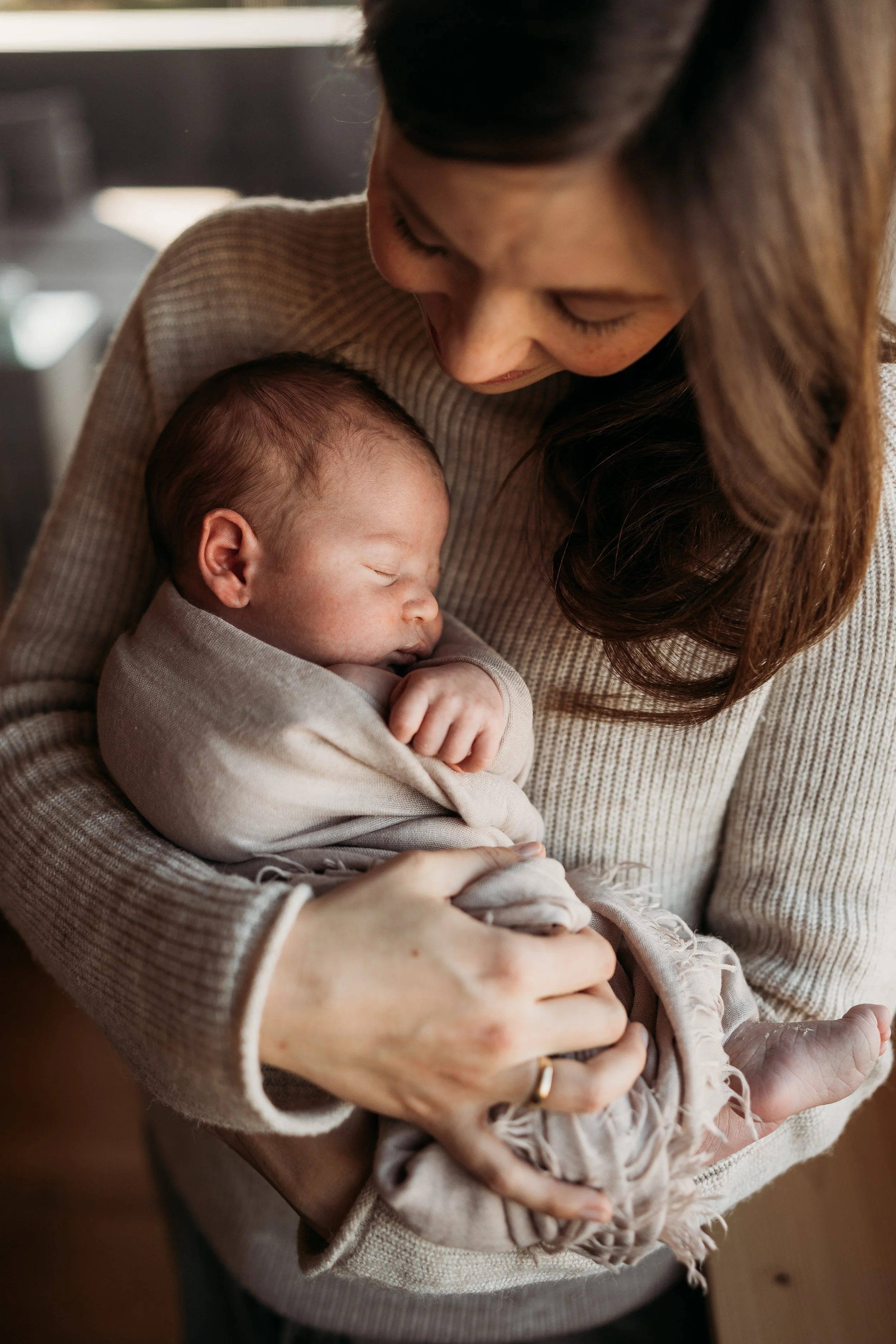 Eine Frau hält ein schlafendes Baby nahe an ihrer Brust und blickt liebevoll auf es.