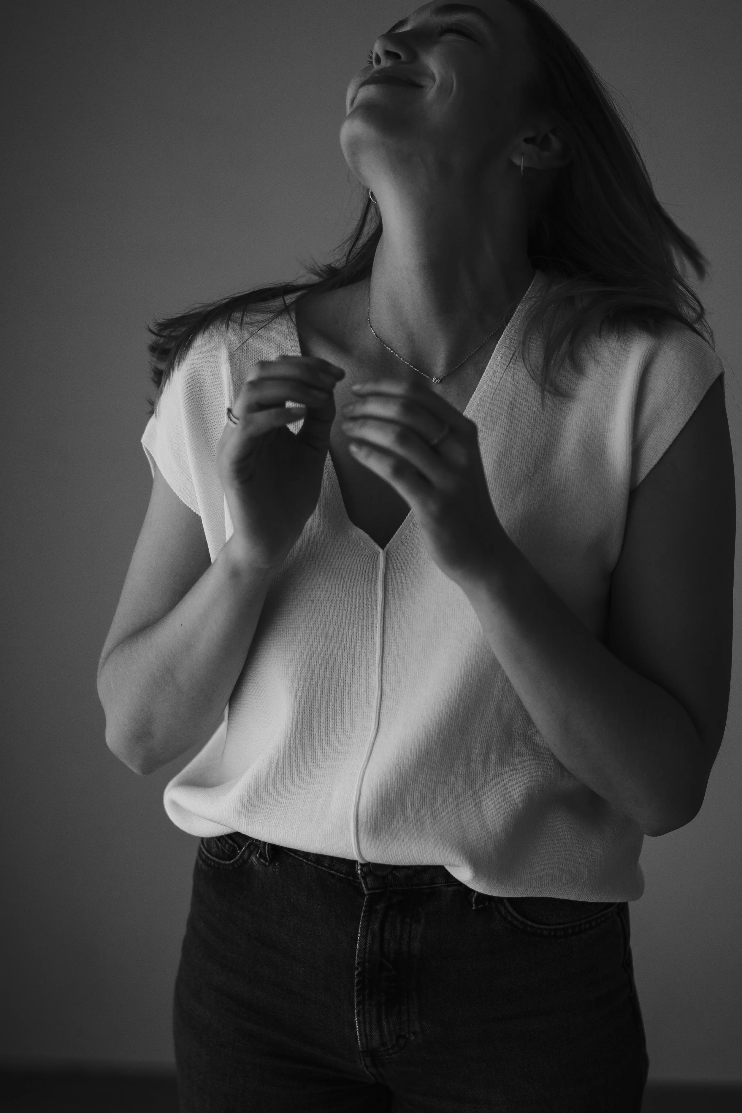 Schwarz-weiß Foto einer lächelnden Frau mit geschlossenen Augen, die ihre Hände vor der Brust hält.