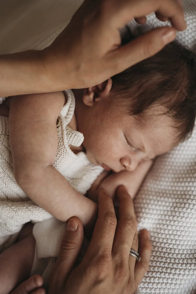 Ein neugeborenes Baby schläft eng an eine Person, die es liebvoll hält, auf einer gestrickten Decke.