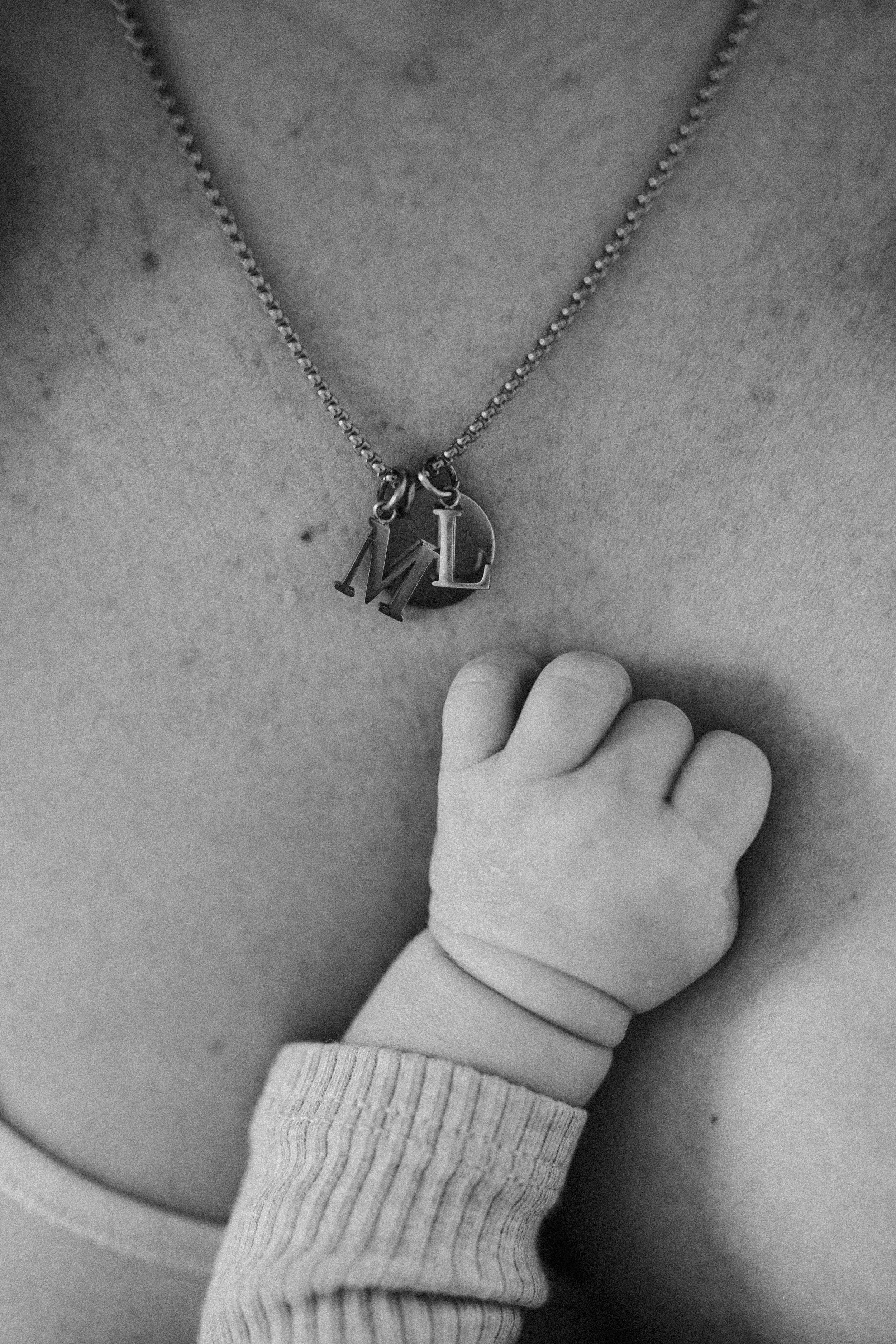 Eine Halskette mit Anhängern mit den Buchstaben M und D, die um den Hals einer Person liegen, während ein Kinderfinger die Brust berührt.