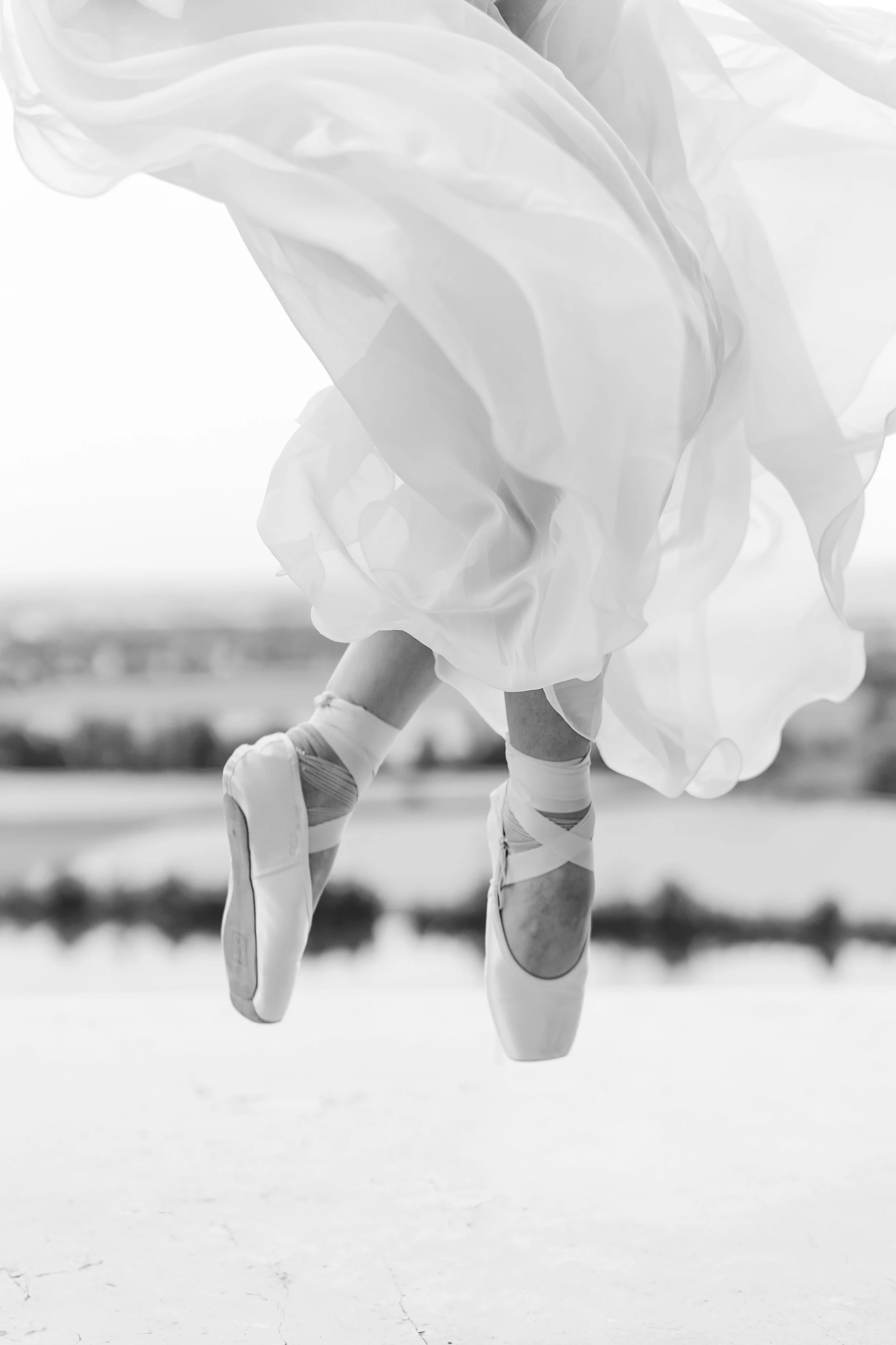 Ballettänzerin tanzt auf Zehenspitzen im Freien, Blick auf halbe Bein, weite geleeartige Kleidung, schwarze und weiße Ballettschuhe, Schwarz-Weiß-Fotografie.