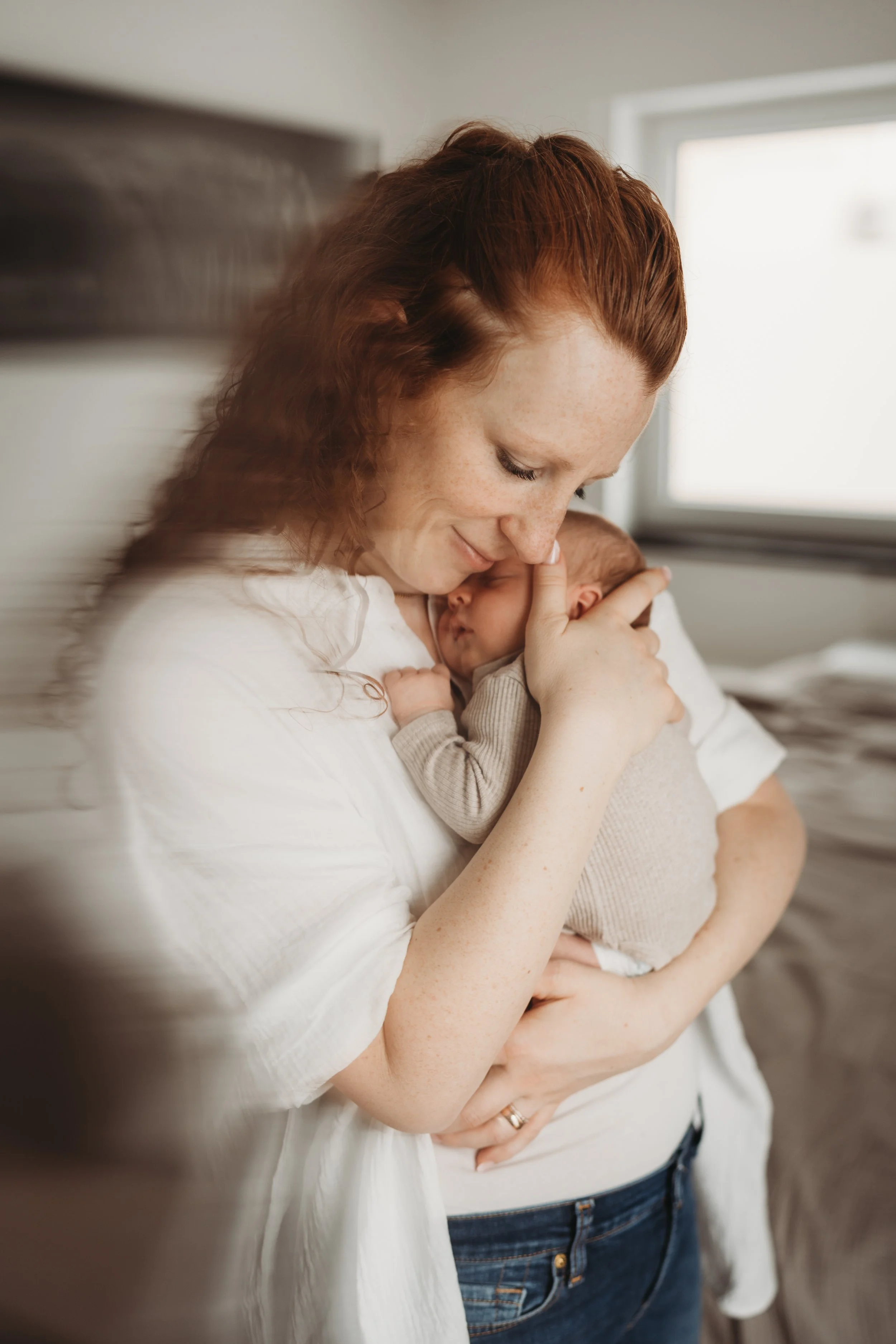 Eine Frau hält ein schlafendes Baby nahe an ihrer Brust, beide haben einen liebevollen Ausdruck.