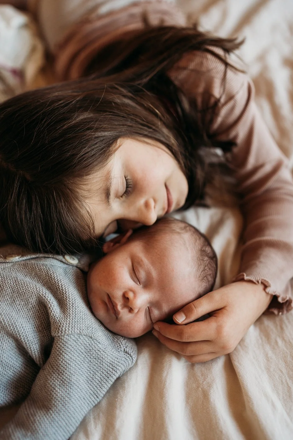 Junge Frau schläft liebevoll mit ihrem neugeborenen Baby auf einem Bett.