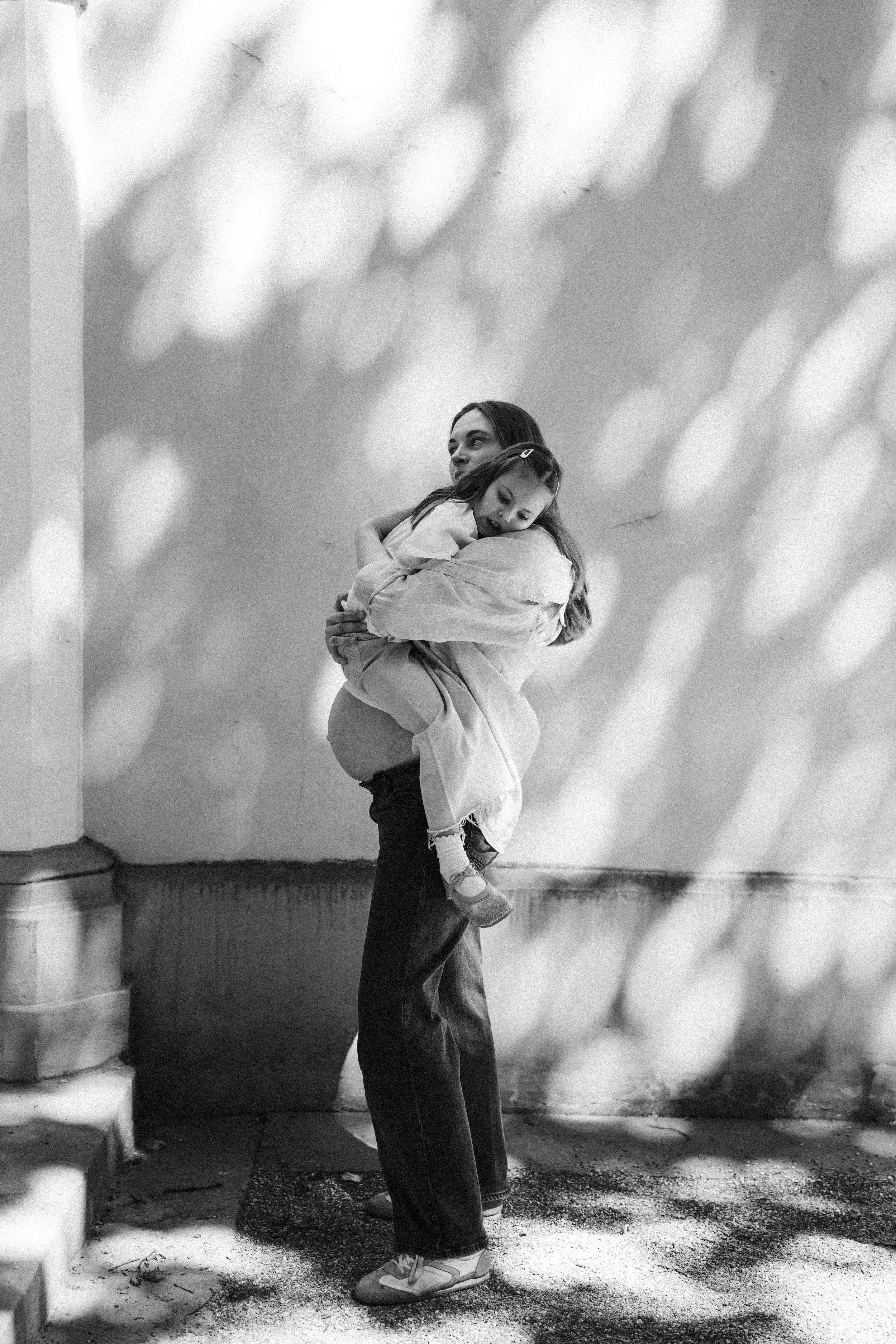 Frau hält ein Kind im Arm, beide lachen, im Hintergrund eine Wand mit bokeh-ähnlichen Lichtern, schwarz-weiß Bild