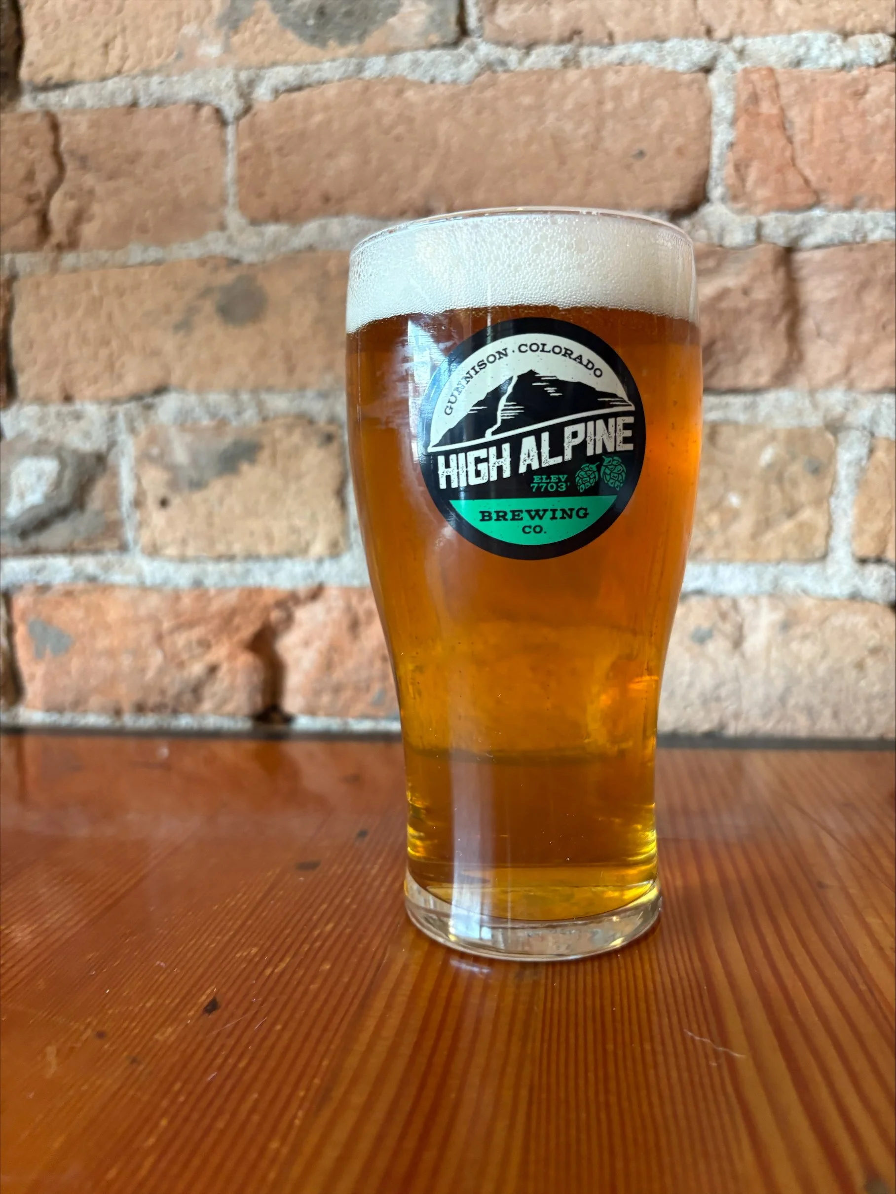 Light straw colored basil beer  in pint glass sitting on a wooden table
