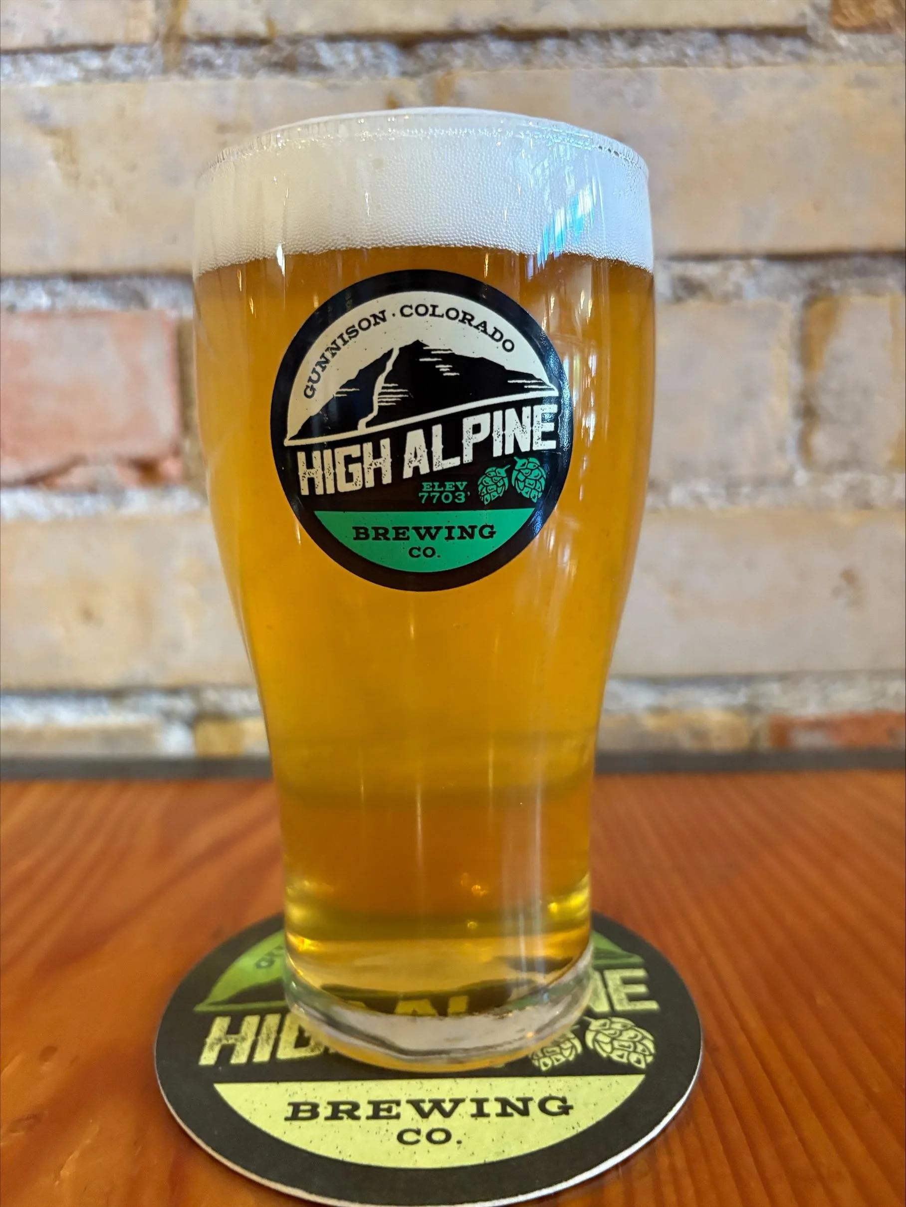 Light straw colored chile beer  in pint glass sitting on a wooden table