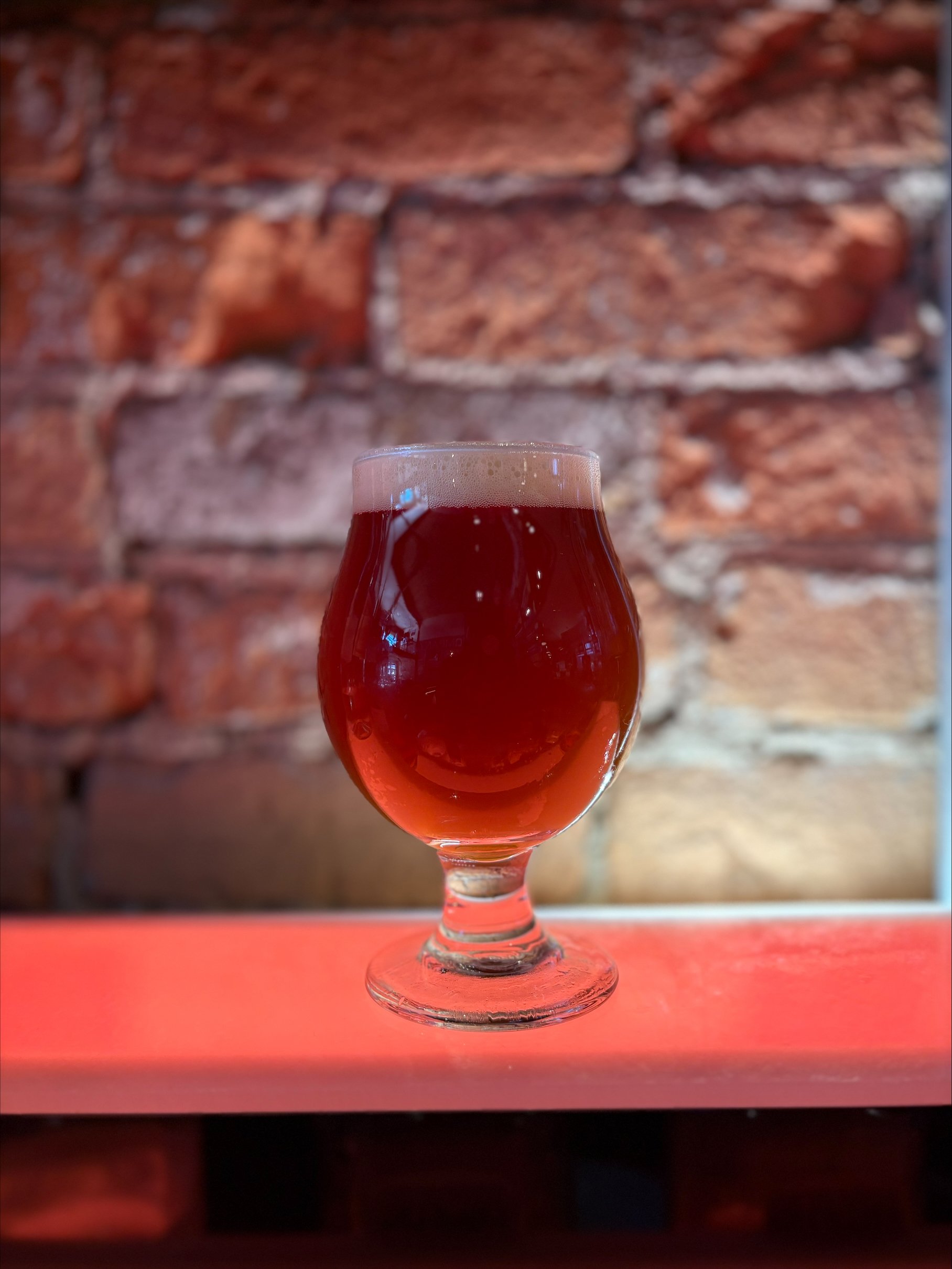 dark amber beer in tulip glass in front of lighted brick