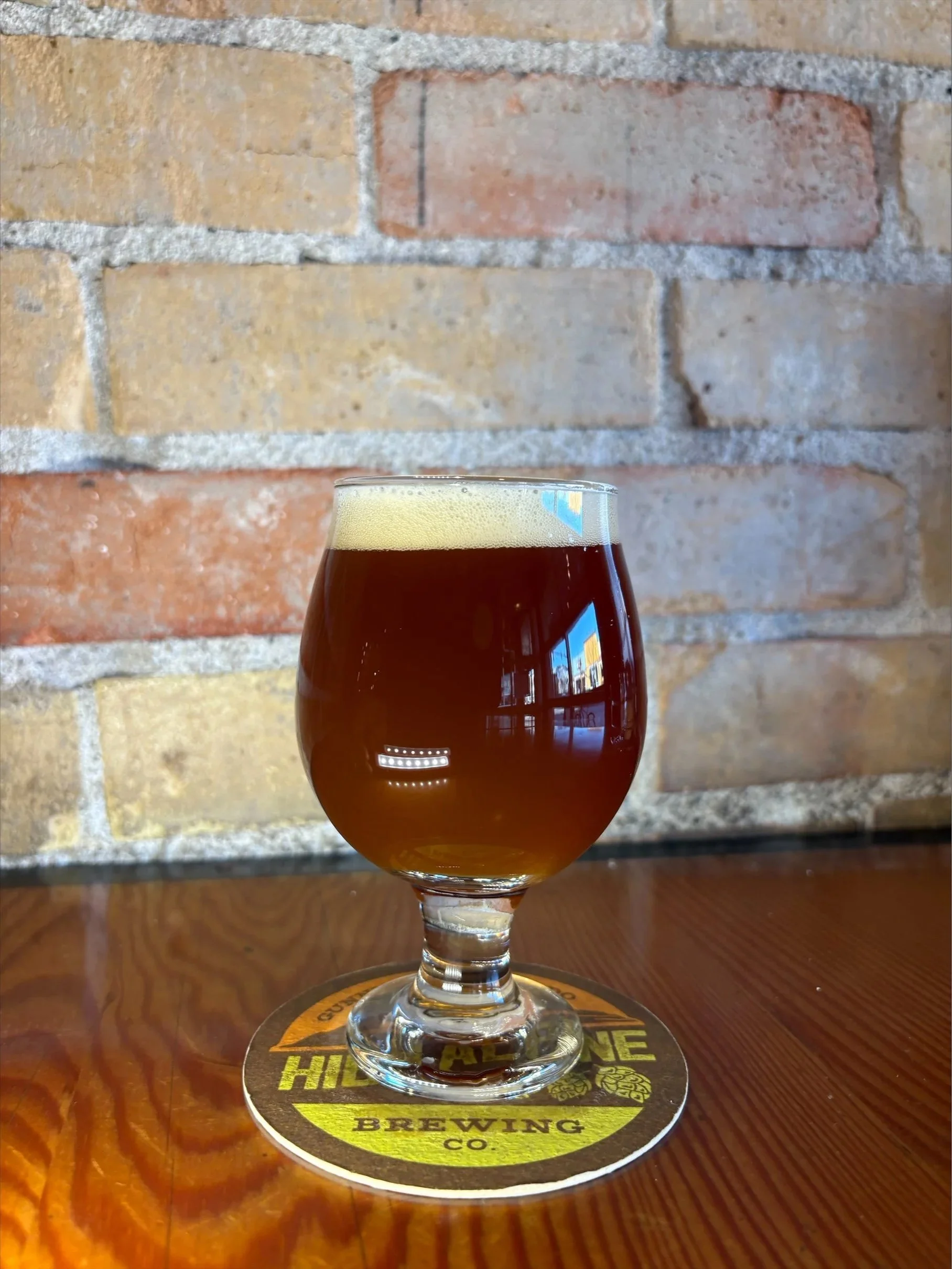 tulip glass of dark amber beer in front of brick wall