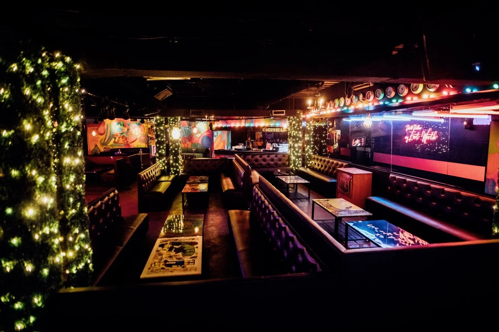 Interior of a dimly lit club with leather booth seating, fairy lights, and colorful wall art.
