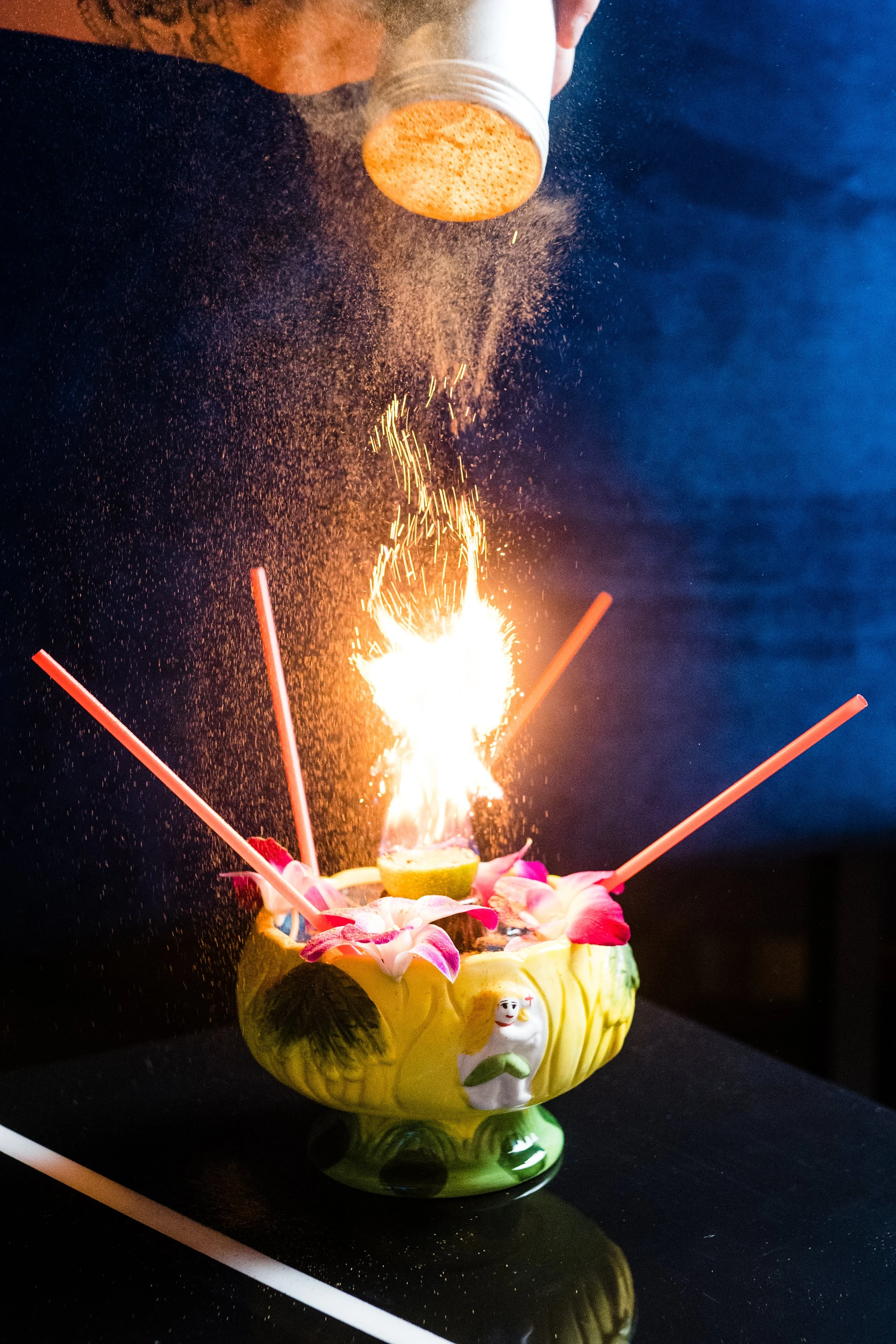 Ceramic bowl with tropical drink, garnished with flowers and straws, ignited at the center.