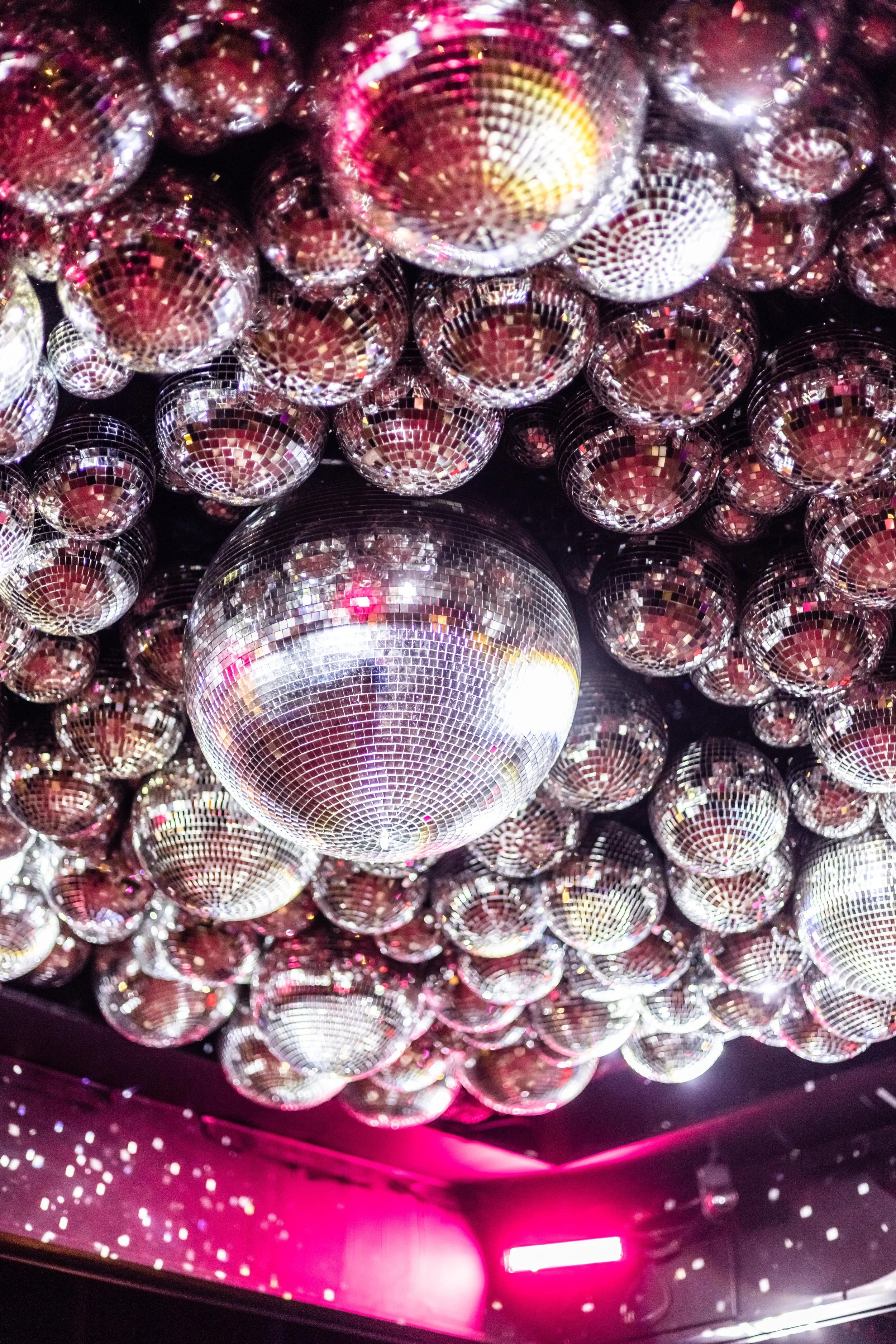 Ceiling filled with multiple shiny disco balls reflecting light in a pink-lit room.