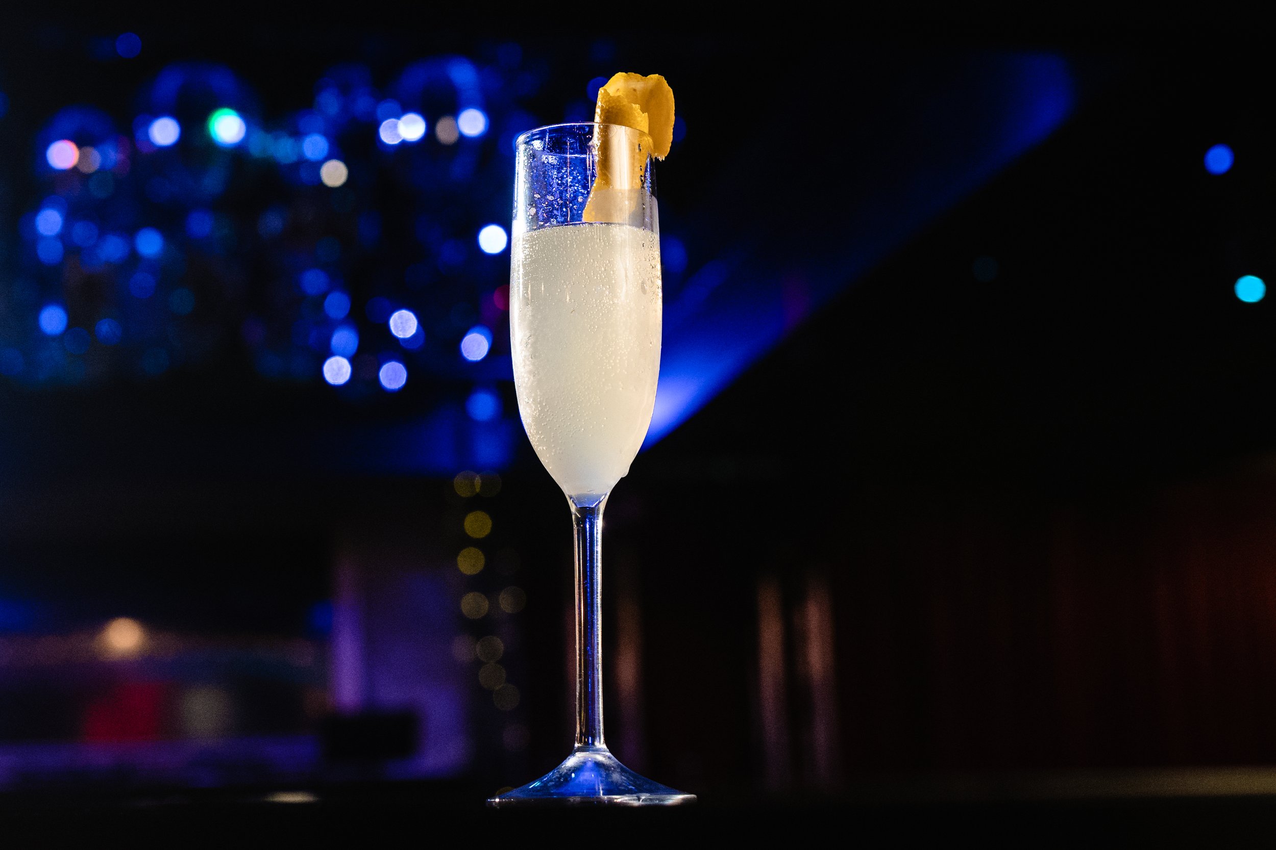 Champagne flute with a lemon twist garnish against a blurred background of blue and purple lights.