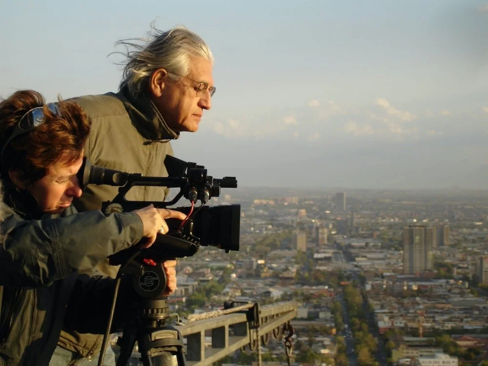Filmmaker Patricio Guzman stands next to a camera operator outside.