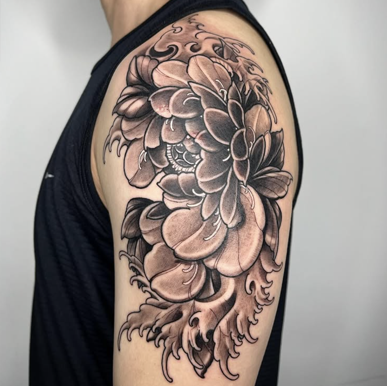 Black and gray floral tattoo on upper arm featuring detailed petals and leaves.