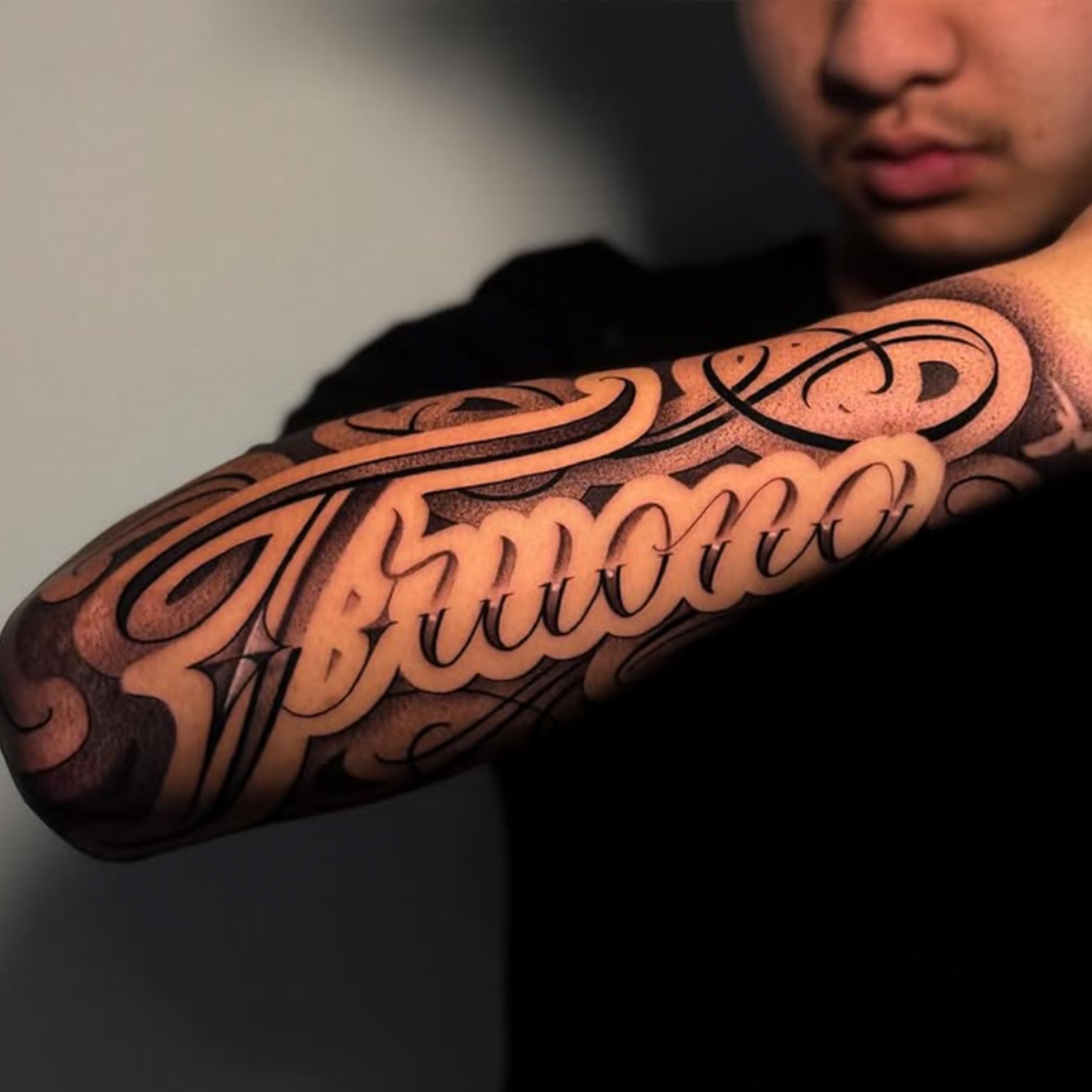 A man showing his tattooed forearm with intricate black cursive lettering.