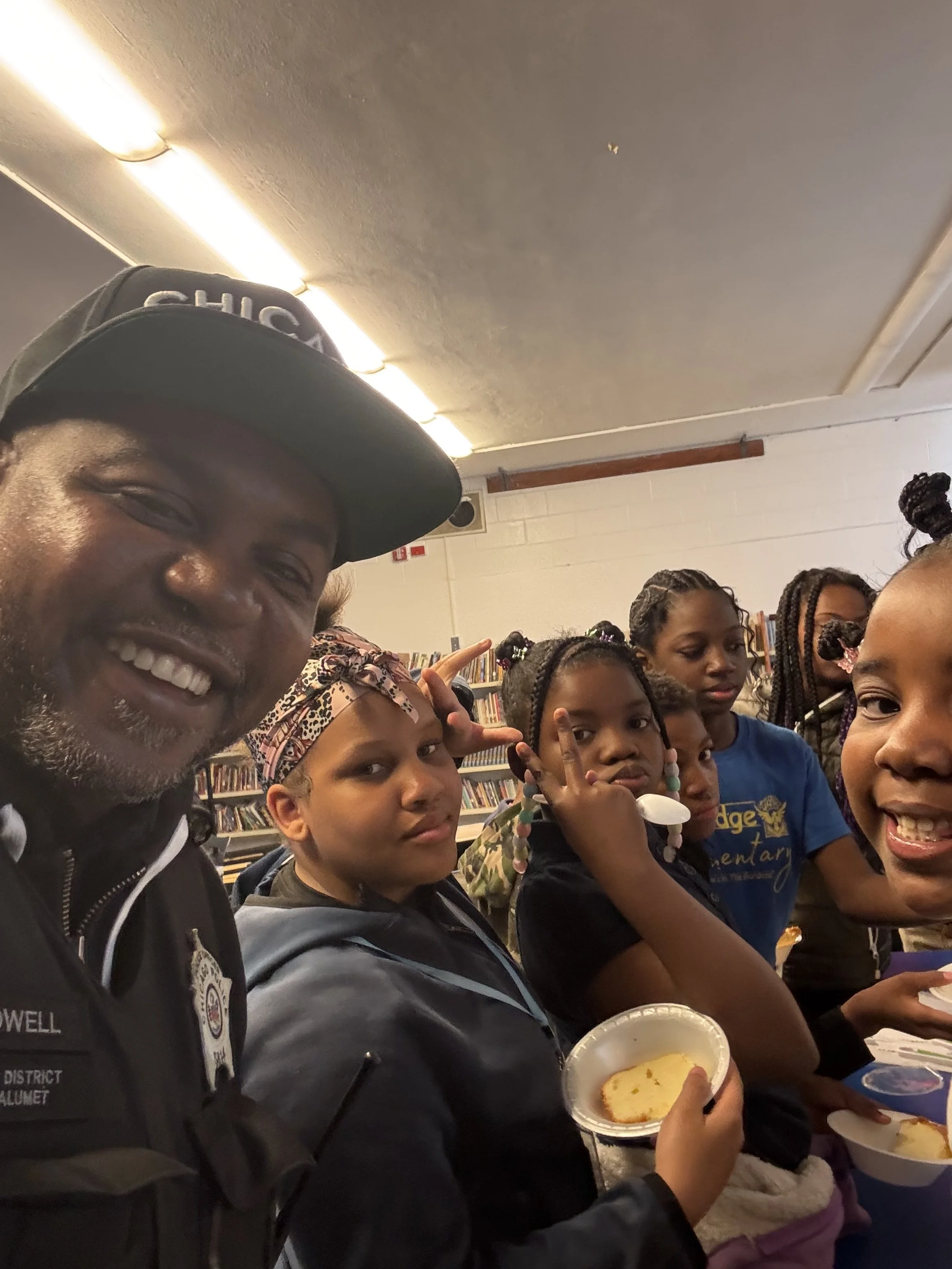A group of children and one adult at a library, some holding slices of cake, with bookshelves in the background.
