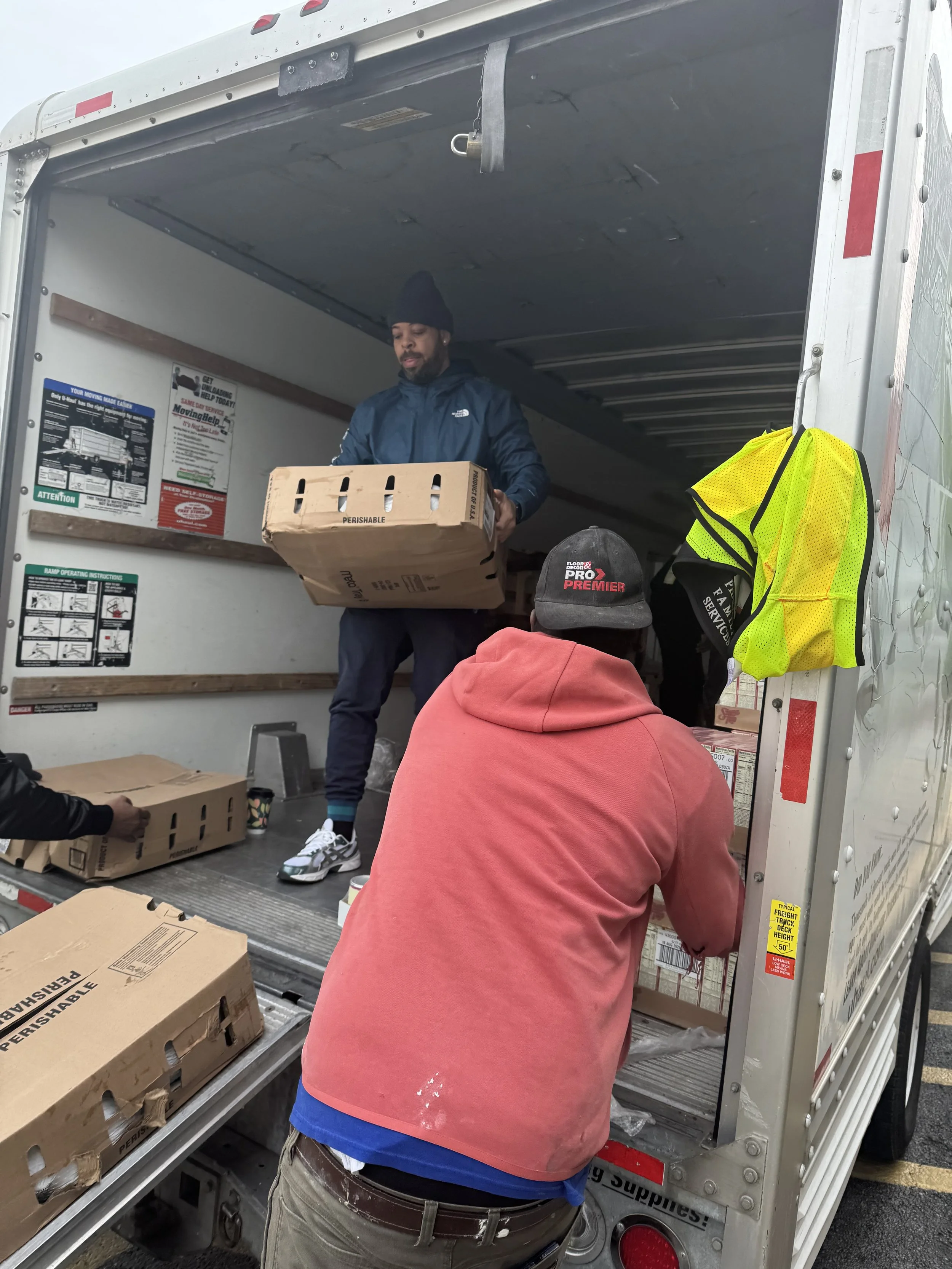 Three men loading boxes into a delivery truck. One man inside the truck, another leaning on the truck, and a third handing a box.