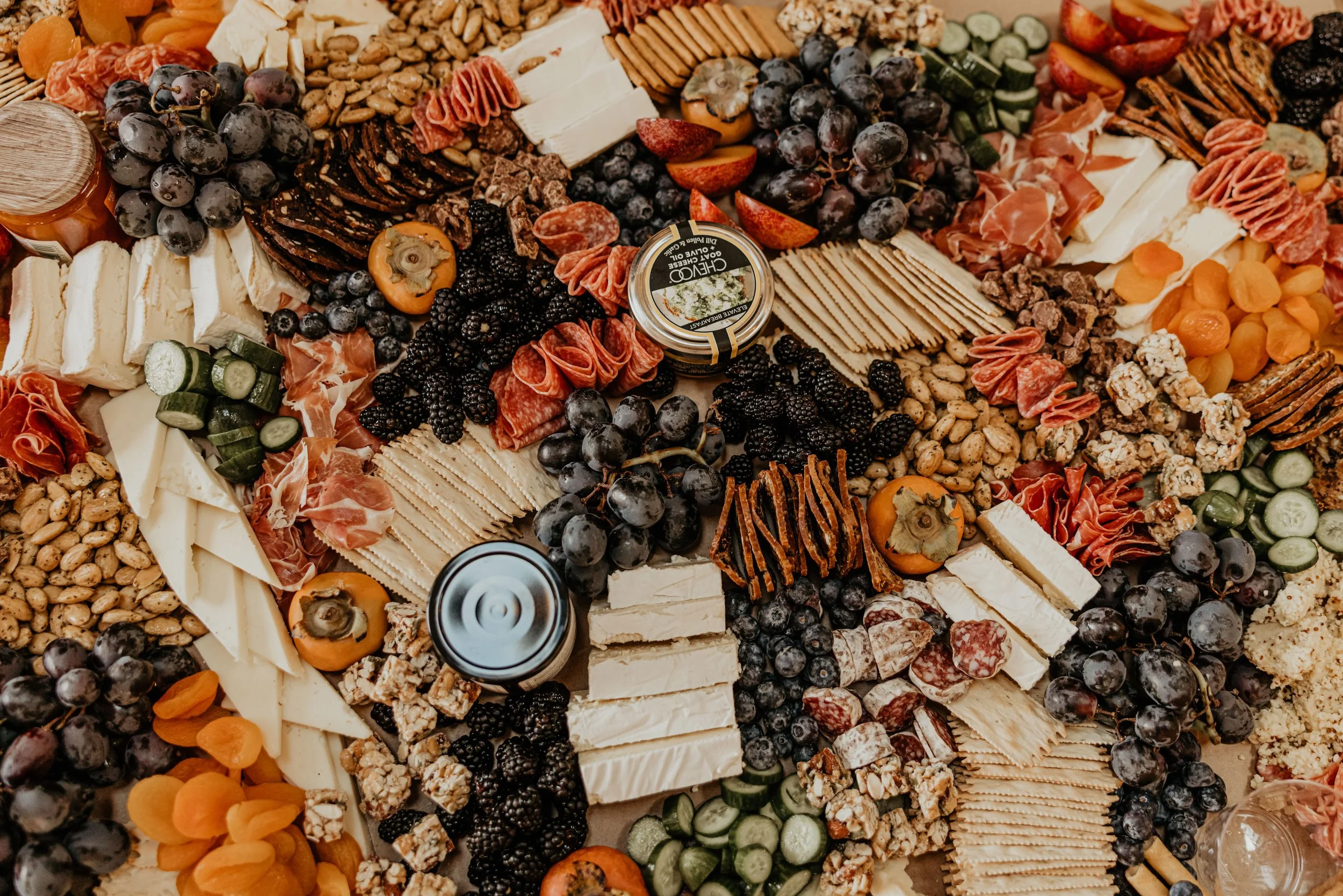 A large cheese and charcuterie board with various cheeses, fruits, crackers, nuts, and cured meats arranged for a gathering.