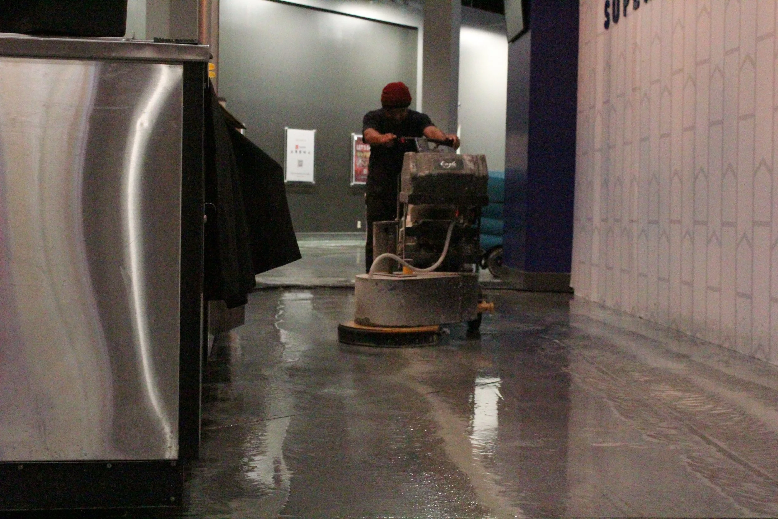 Floor in kitchen being polished by worker with large industrial machine.