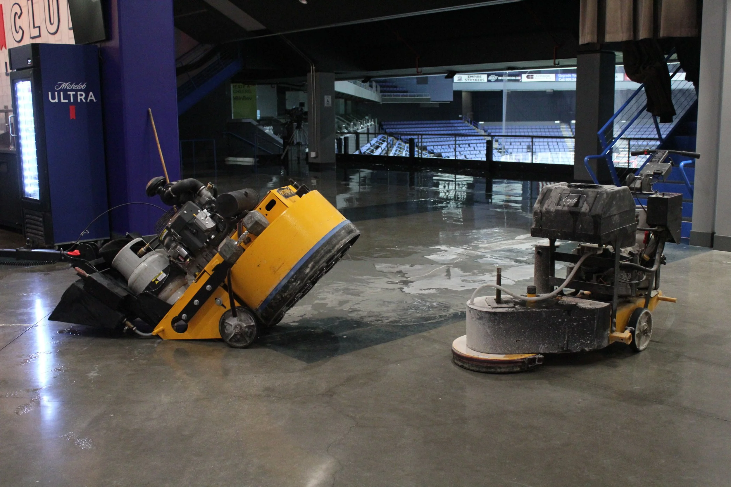 Concrete floor partially finished being polished with two large machines.