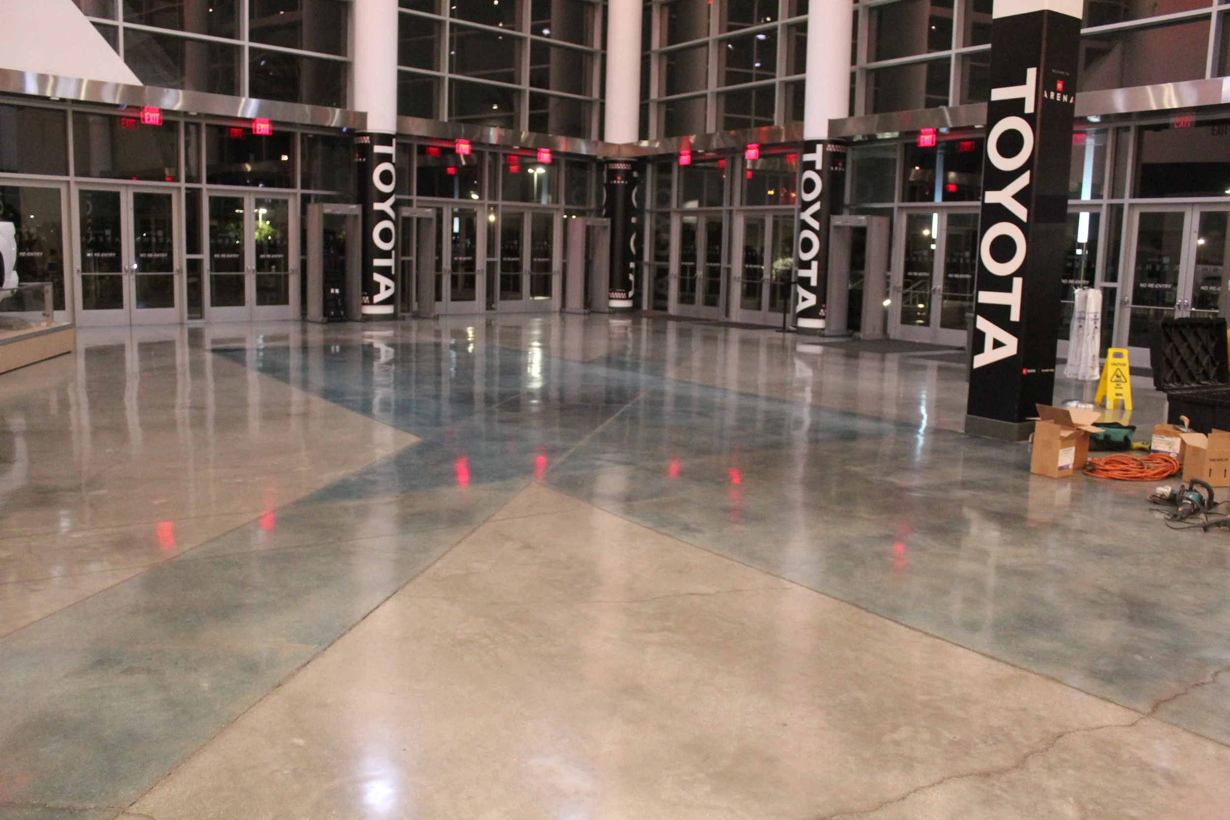 Polished floors in lobby of Toyota Center with glass windows and doors in the back. There's some visible cleaning equipment in the corner.