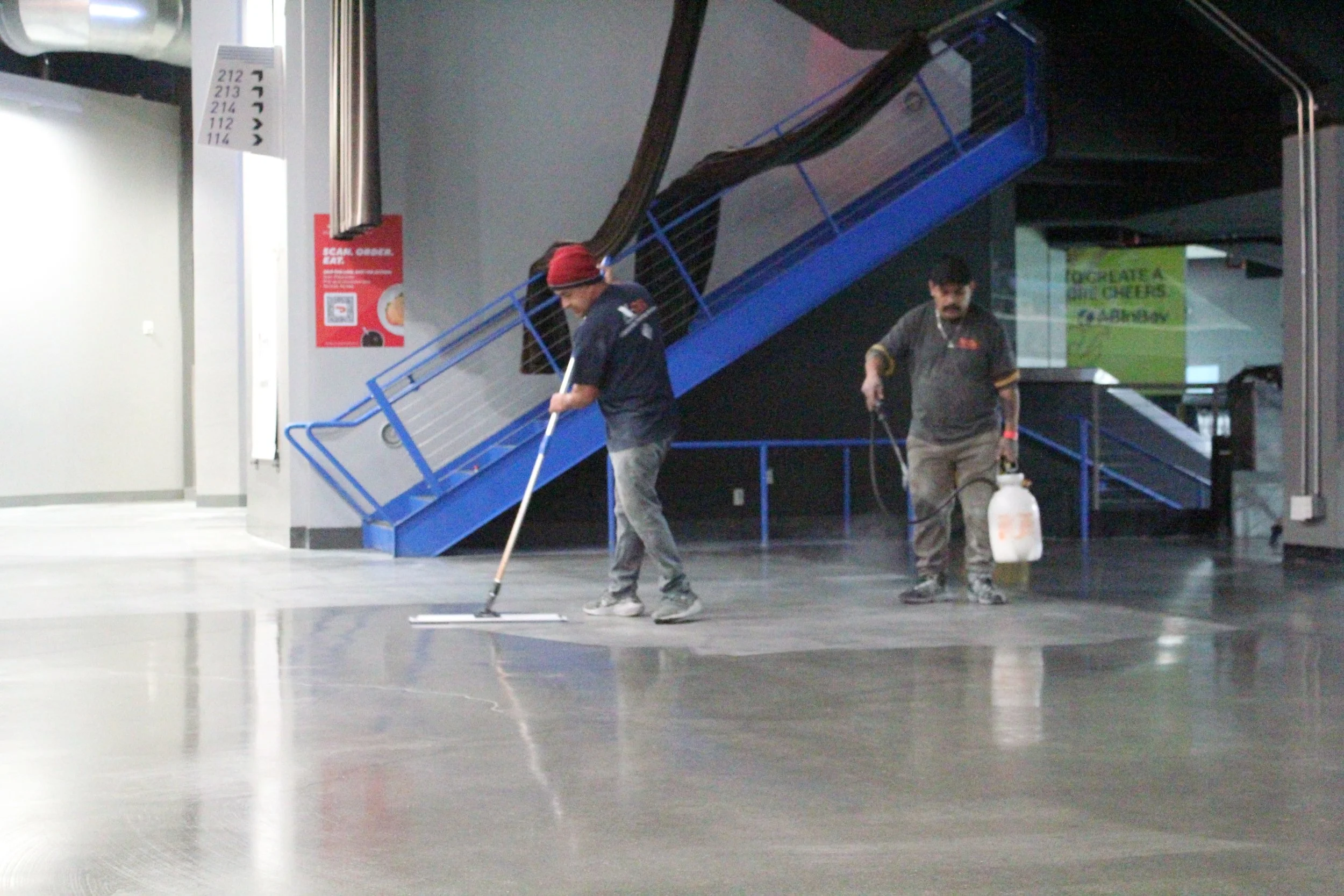 Concrete floors in the Toyota Arena being resealed with a solution by two workers.