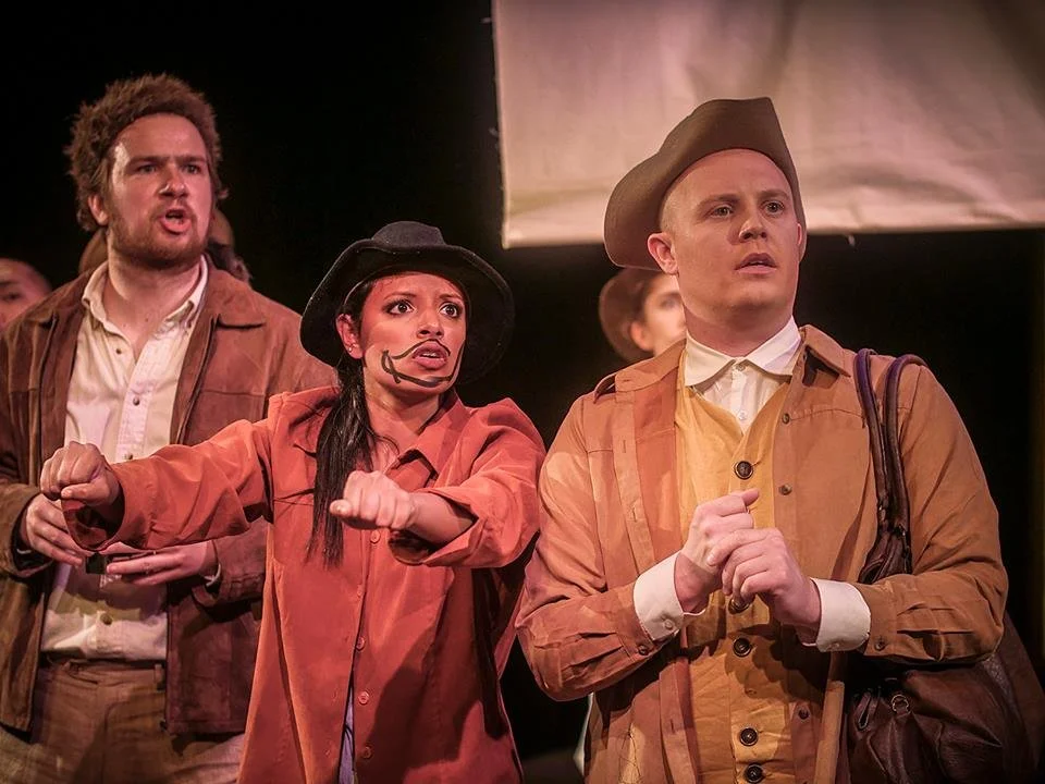 Three actors on stage in costume, appearing to perform in a play, with intense and expressive facial expressions.