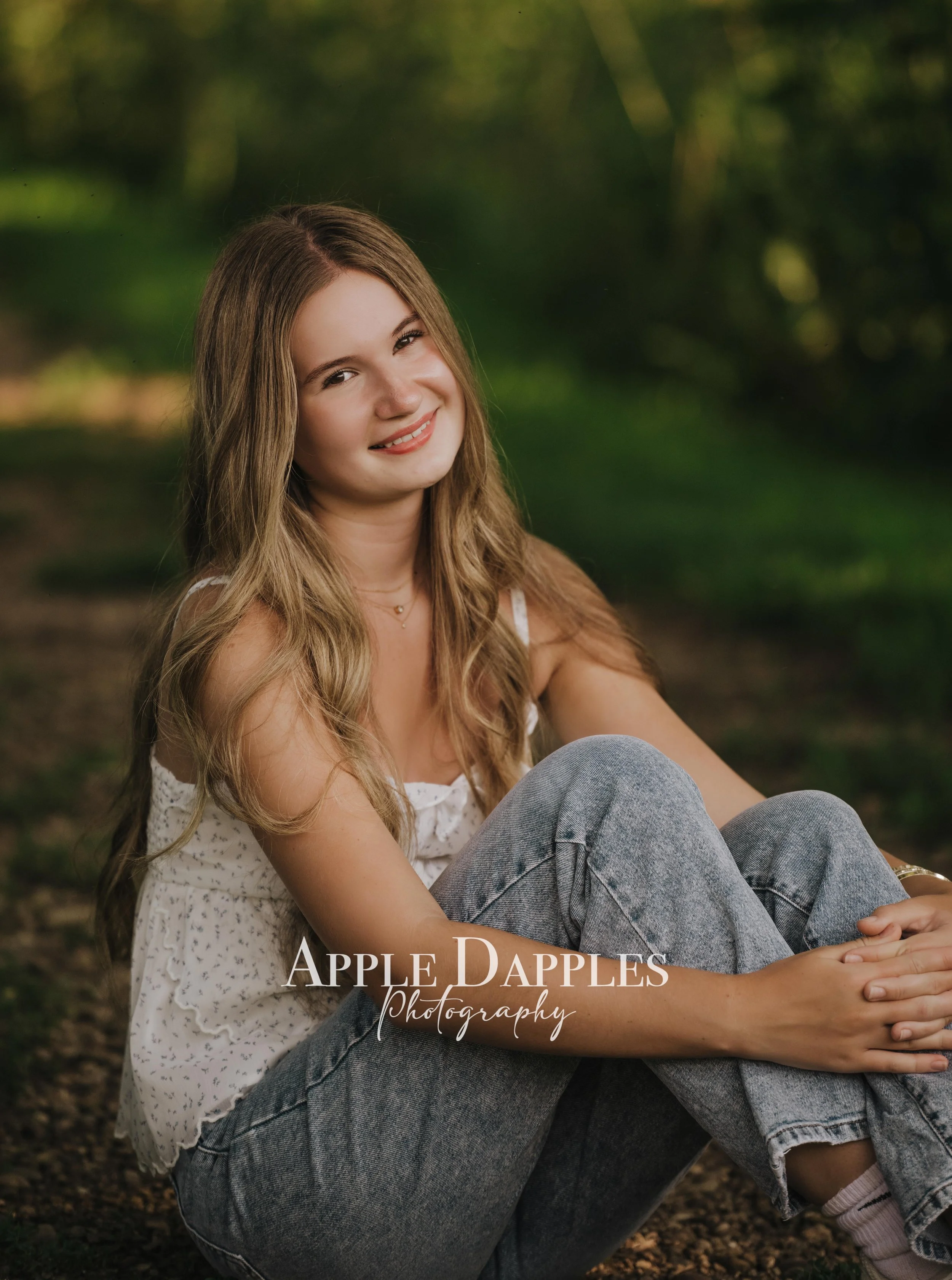 High school senior girl sitting on a tree-covered path during an outdoor senior photo sessio